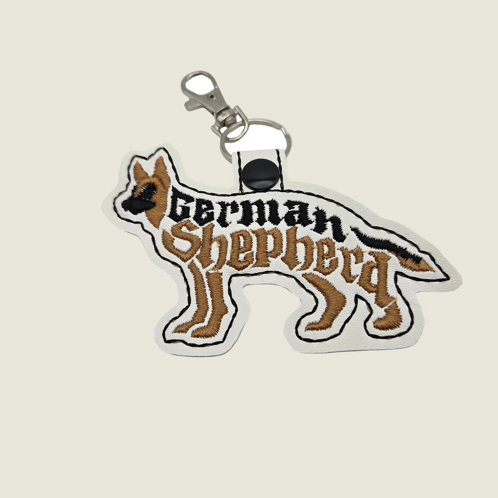 Embroidered German Shepherd keychain in white, featuring the breed's silhouette and name in black and brown.