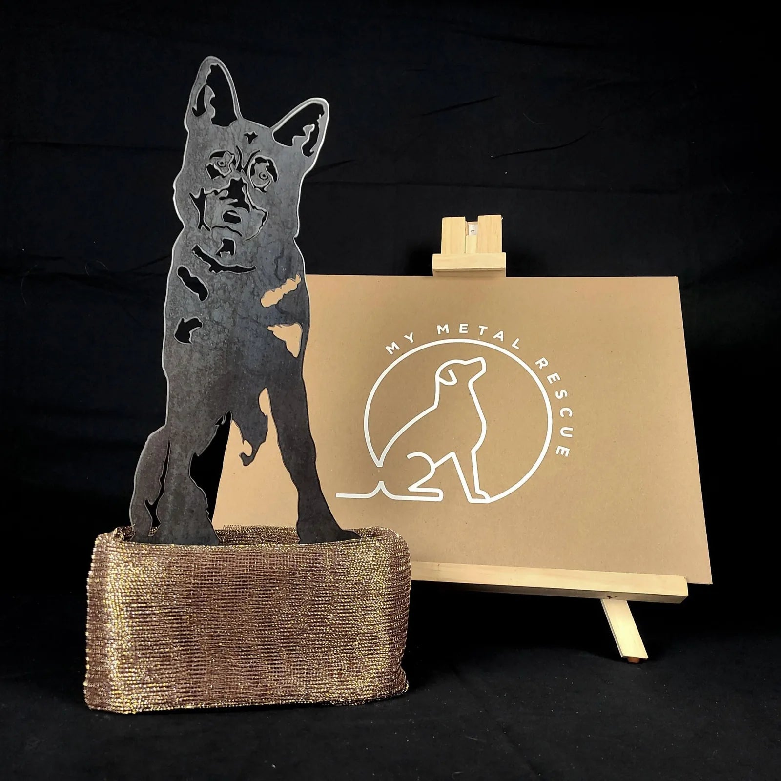 German Shepherd metal silhouette stands on a textured bronze base, showcasing intricate cut details against a black backgr...