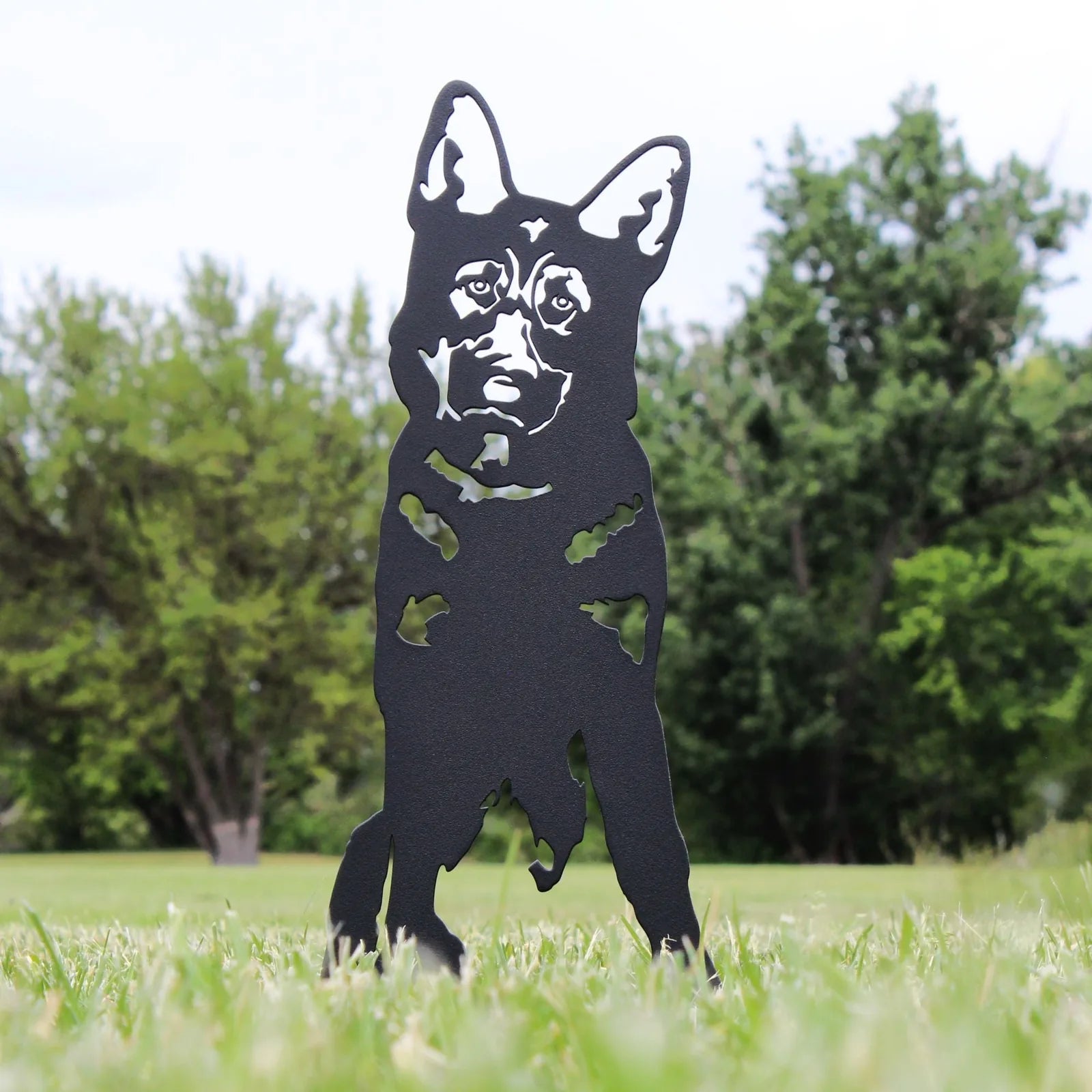 German Shepherd silhouette in matte black metal standing in grass, surrounded by green trees, showcasing intricate detailing.