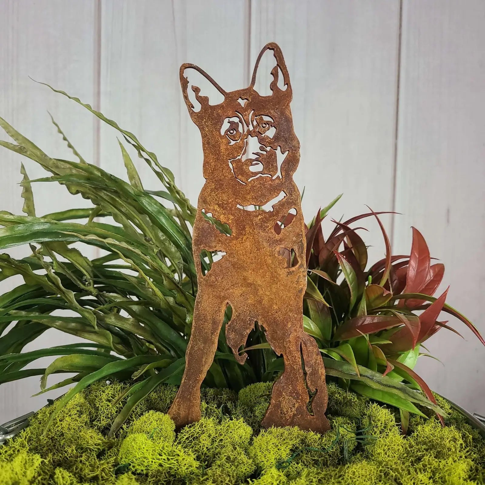 German Shepherd silhouette made of rusted Corten steel, featuring cut-out details, surrounded by green plants.