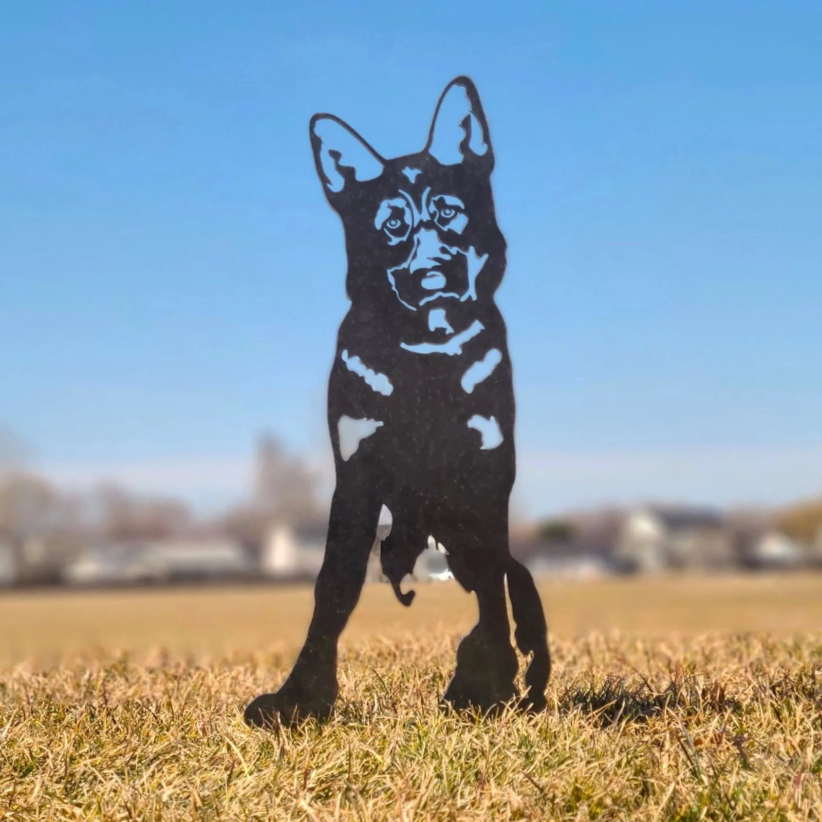 Black metal silhouette of a German Shepherd standing in grass under a clear blue sky, showcasing detailed features.