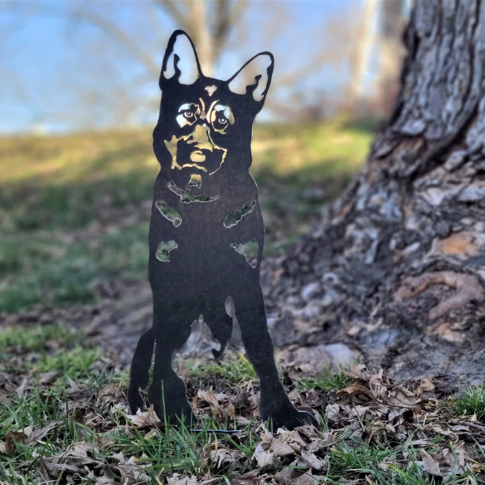 Black German Shepherd metal silhouette standing in grass among fallen leaves, showcasing detailed cutouts and standing pro...