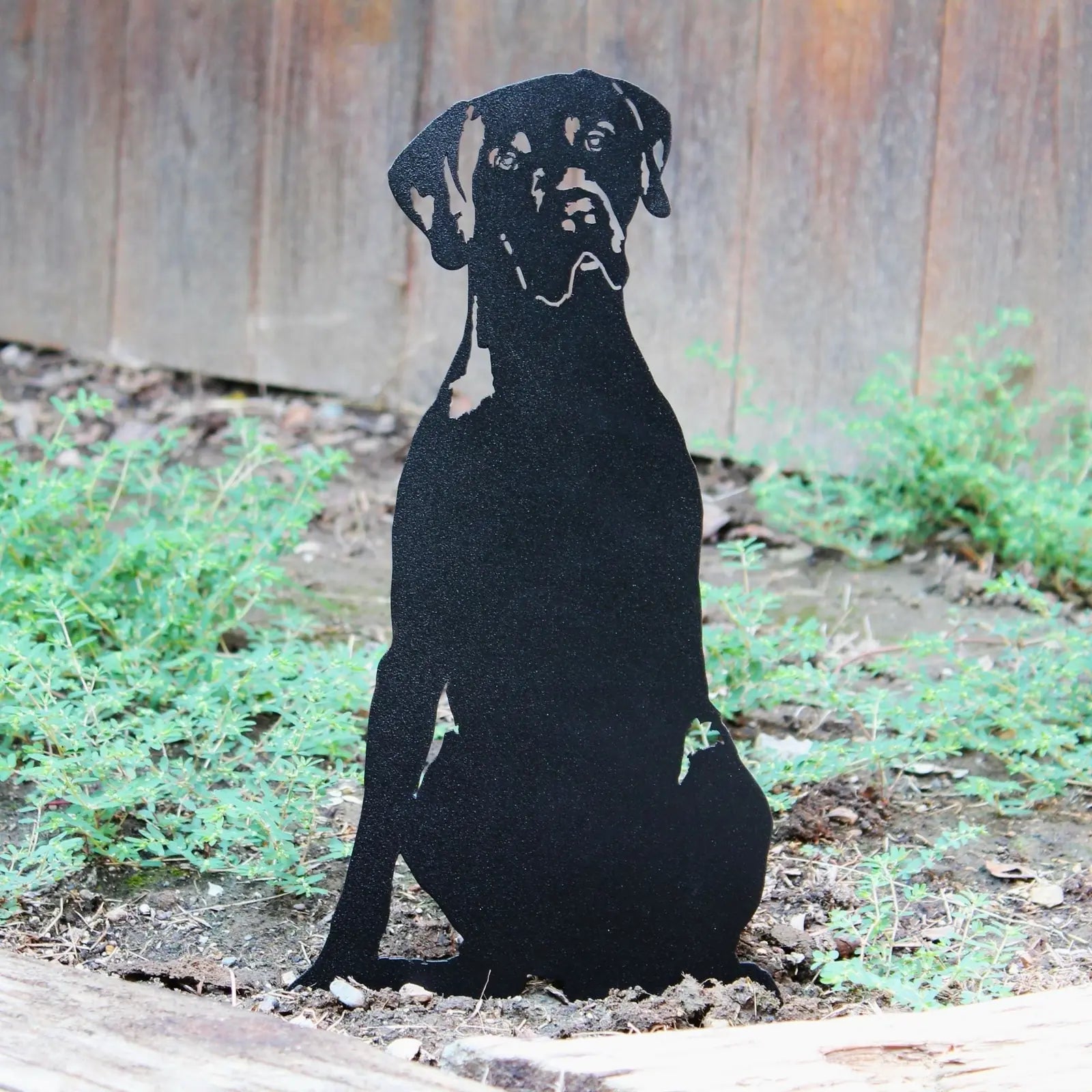 Black metal silhouette of a German Shorthaired Pointer sitting in a garden, surrounded by greenery.