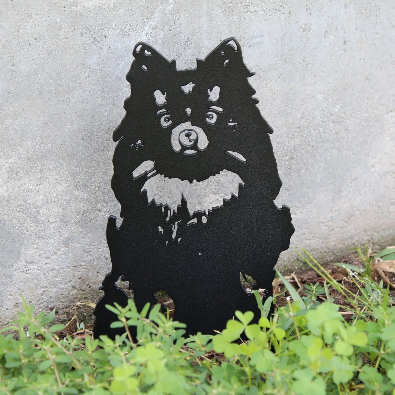 Black metal silhouette of a German Spitz against a gray background, surrounded by greenery. Ideal for dog lovers.