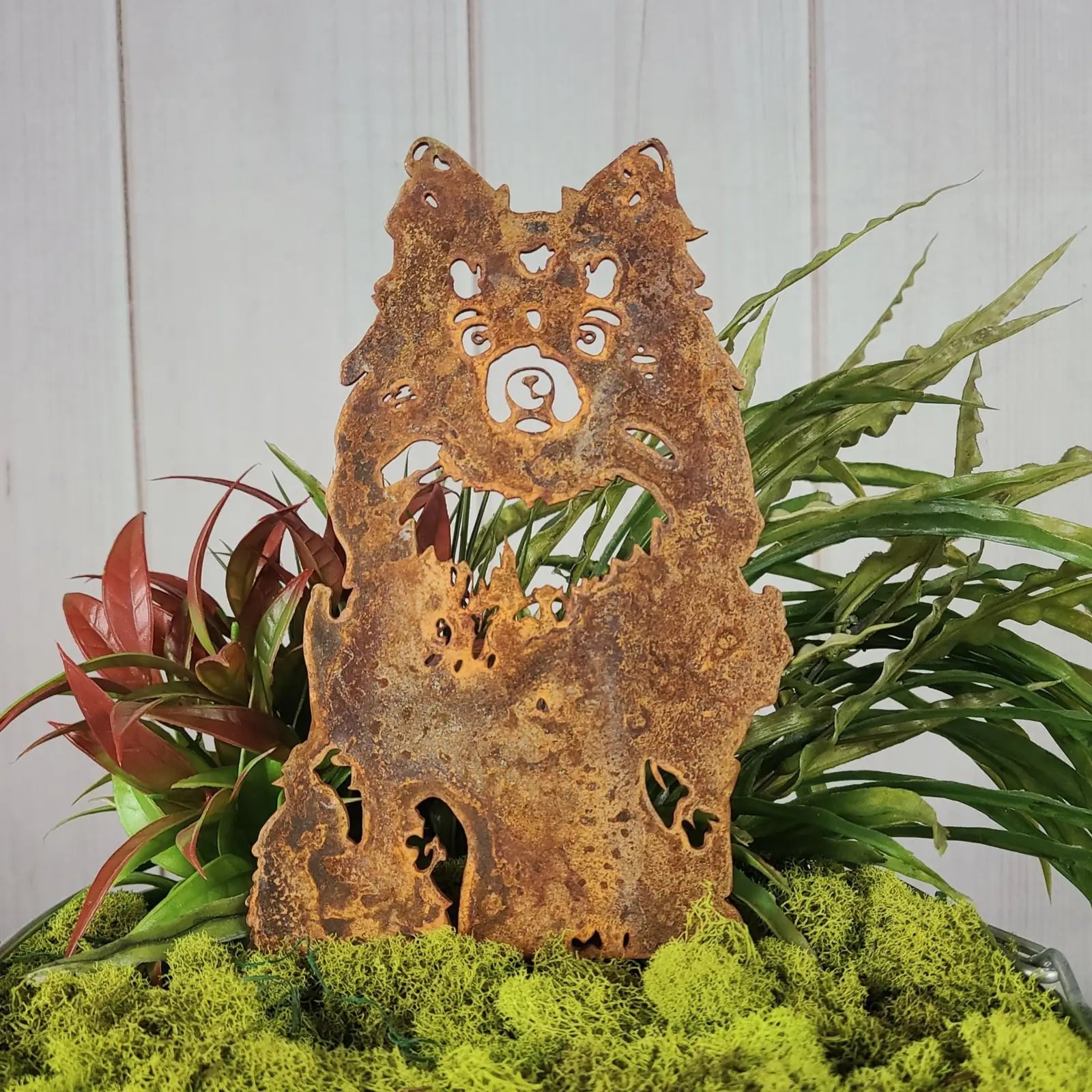 Rusty Corten steel silhouette of a German Spitz dog, surrounded by vibrant greenery and moss.
