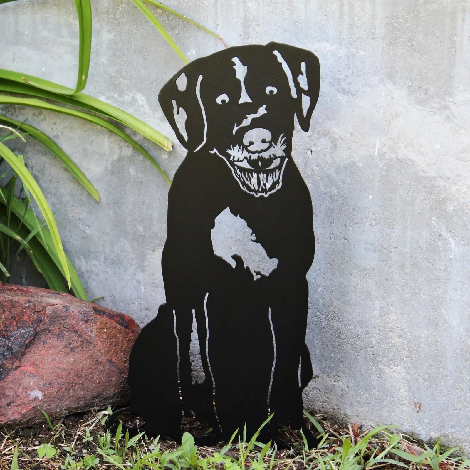 Black metal silhouette of a German Wirehaired Pointer sitting beside rocks and greenery, designed for outdoor decor.
