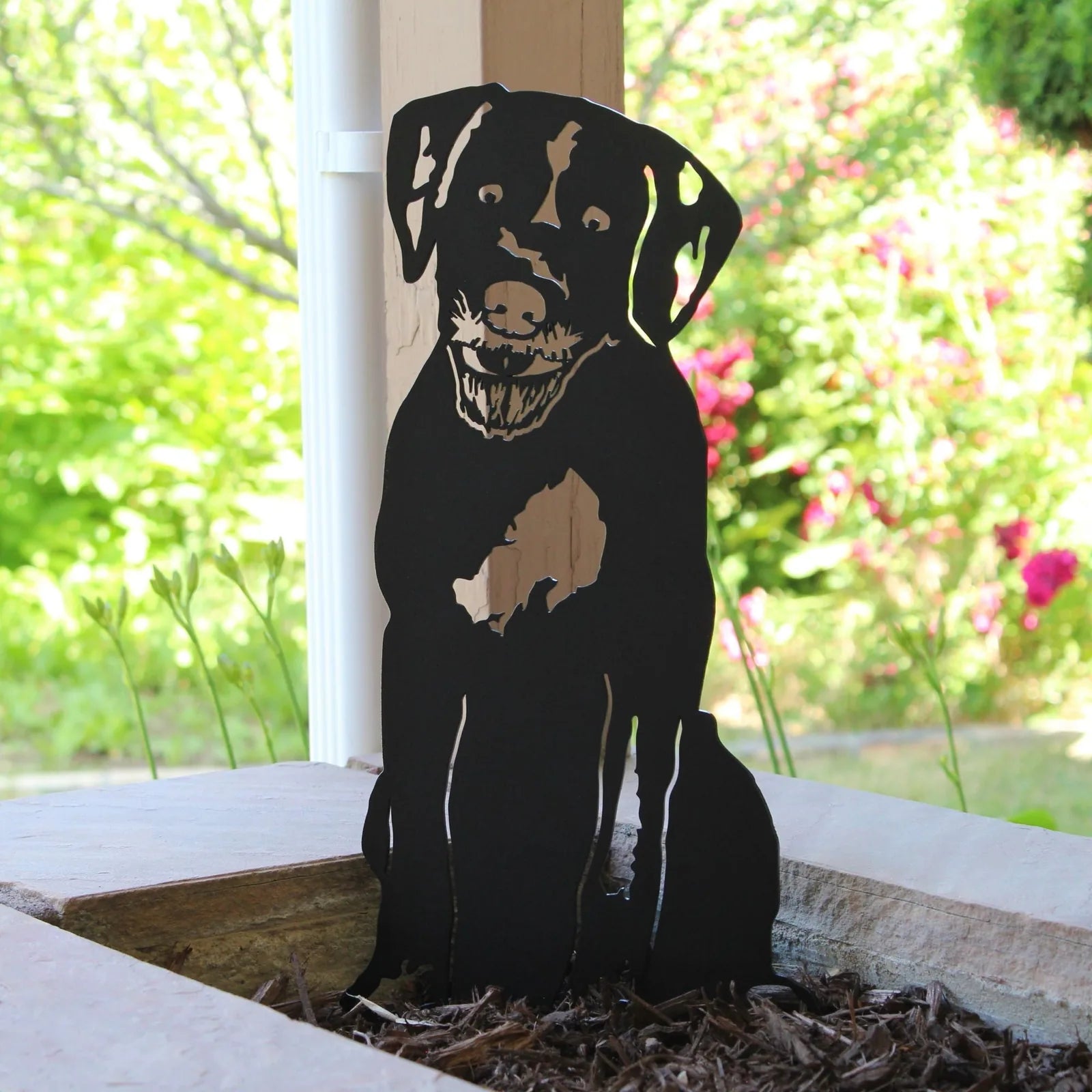 Black metal silhouette of a happy dog sitting, set against a vibrant garden backdrop. Perfect for outdoor decor.