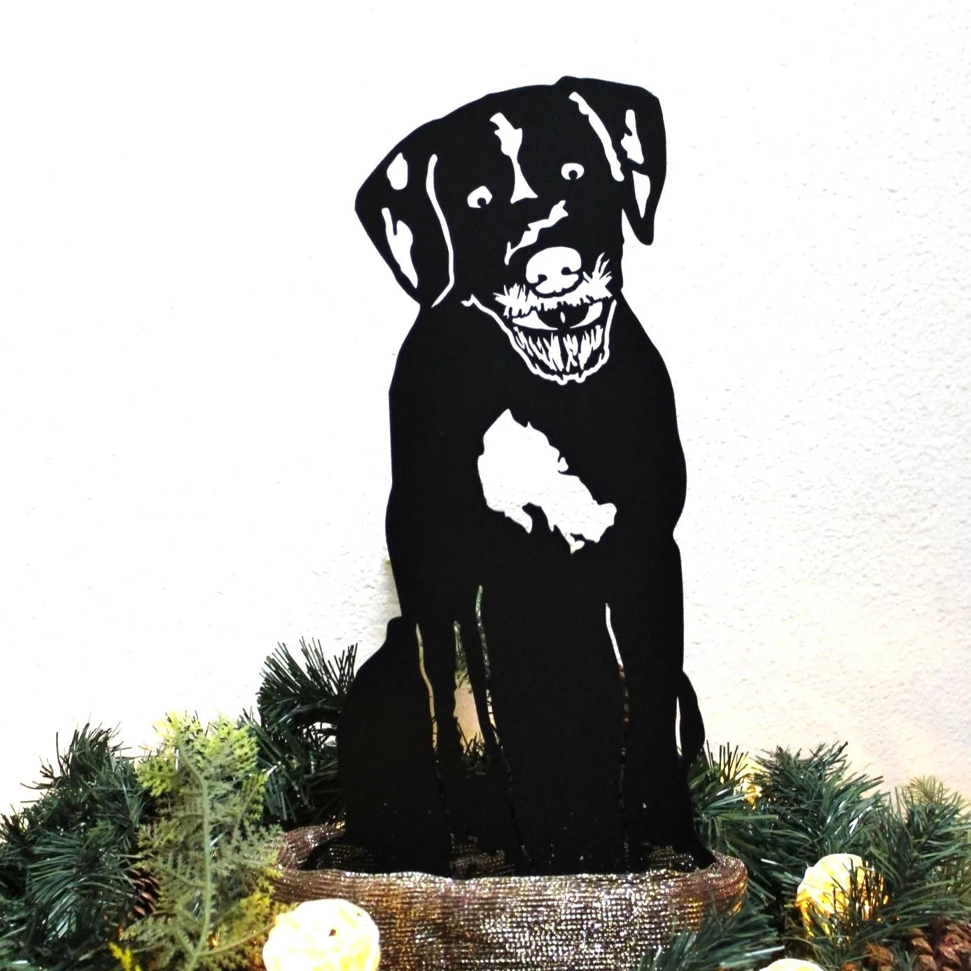 Black metal silhouette of a dog sitting, featuring playful expression, surrounded by greenery. Perfect for outdoor decor.