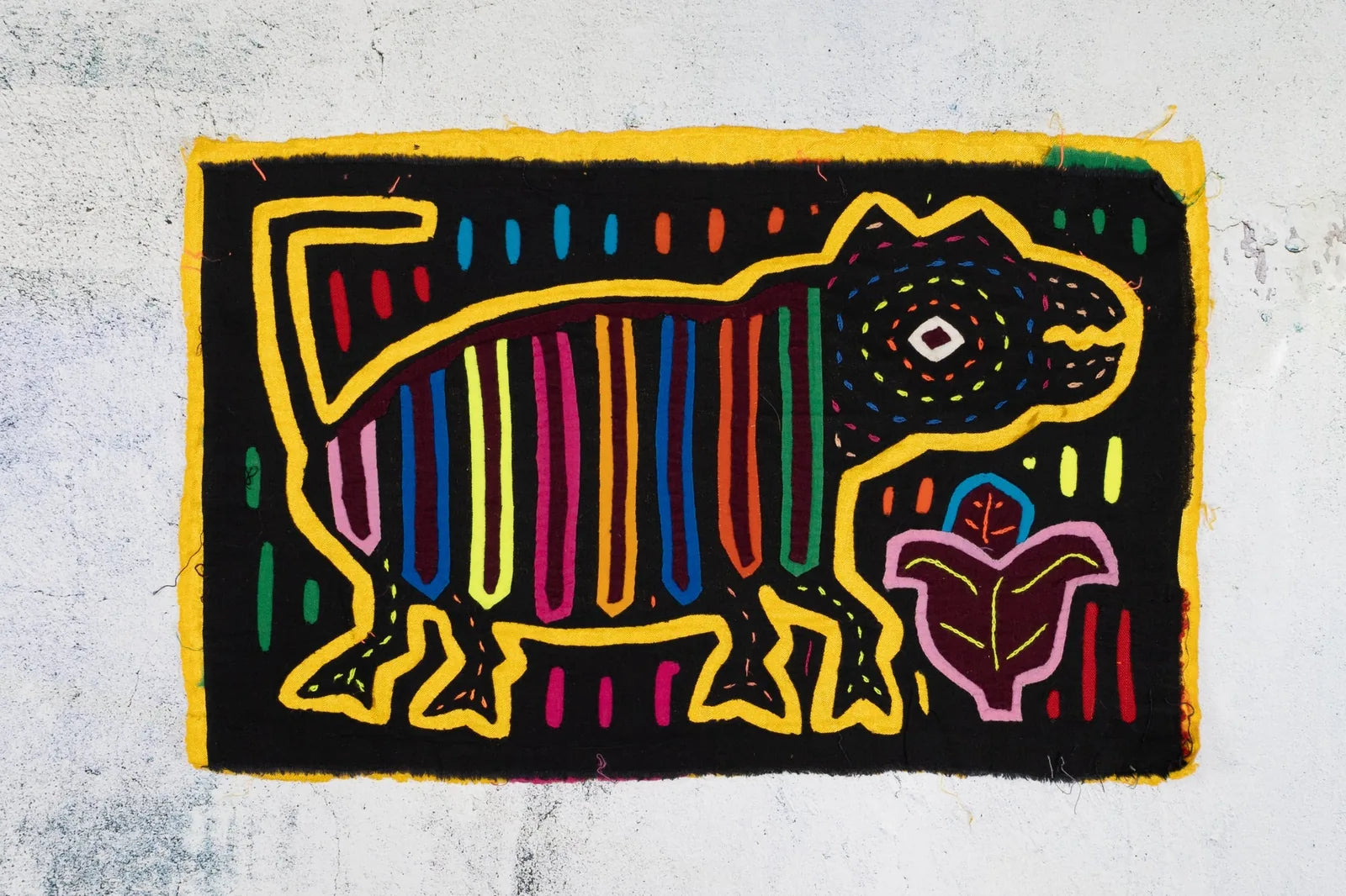 Colorful hand-stitched Mola featuring a playful dog design on a black background, with vibrant geometric patterns.
