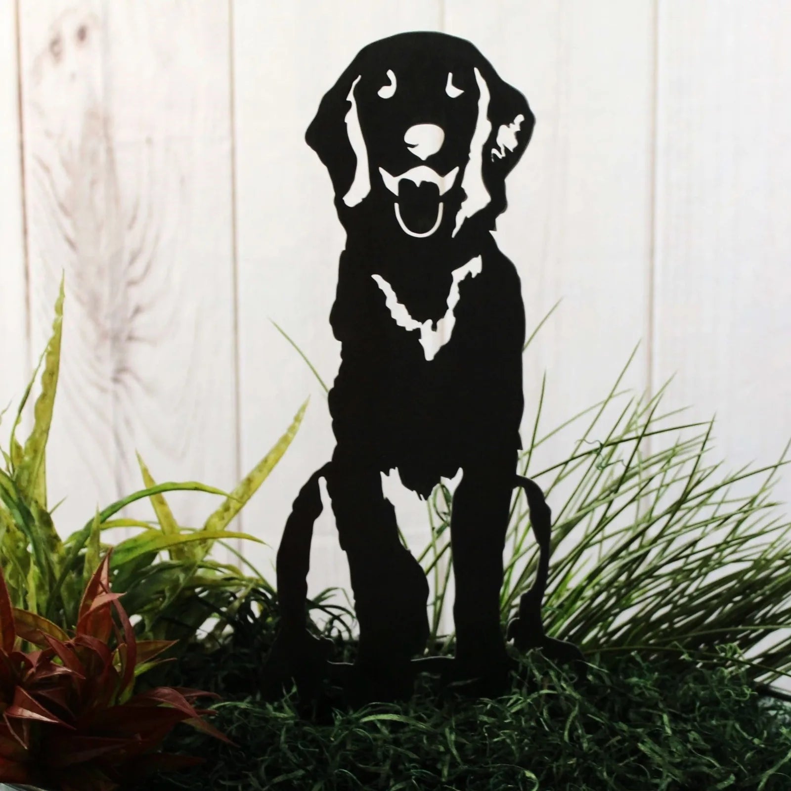 Handcrafted black metal silhouette of a sitting Golden Retriever, surrounded by green foliage and decorative grass.