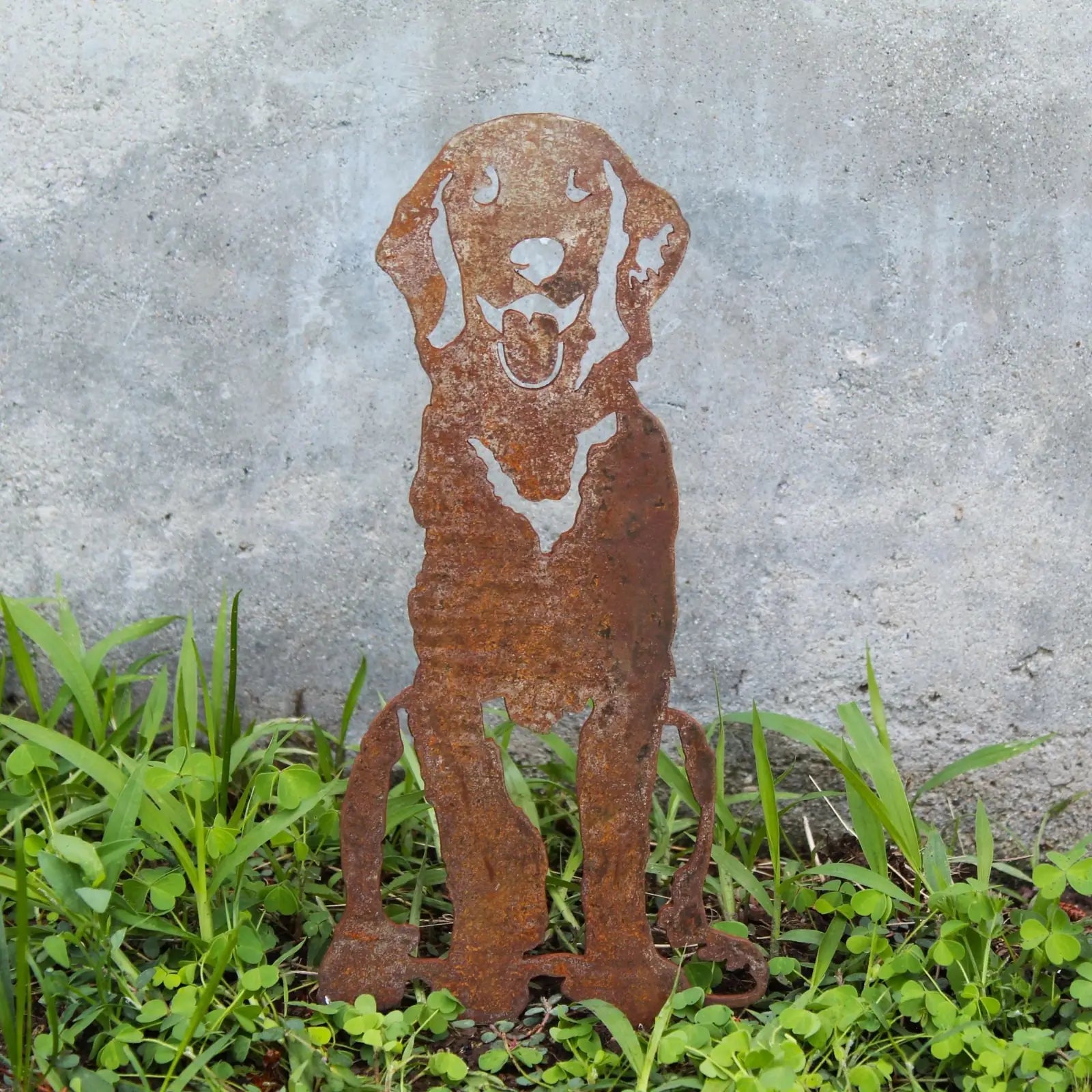 Rusty metal silhouette of a seated Golden Retriever, surrounded by green grass, showcasing handcrafted dog décor.