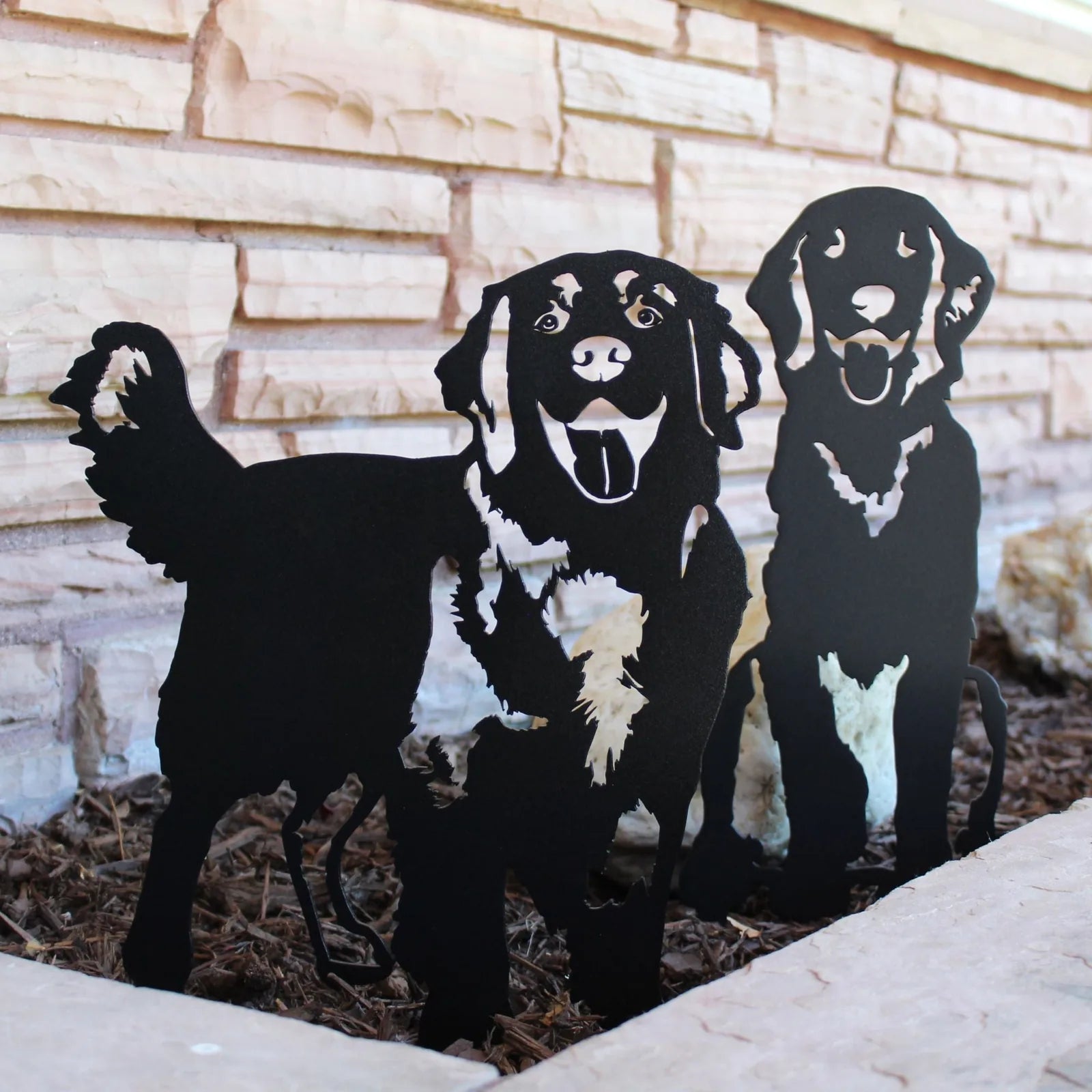 Black metal silhouette of two Golden Retrievers standing in mulch, showcasing playful expressions and detailed features.