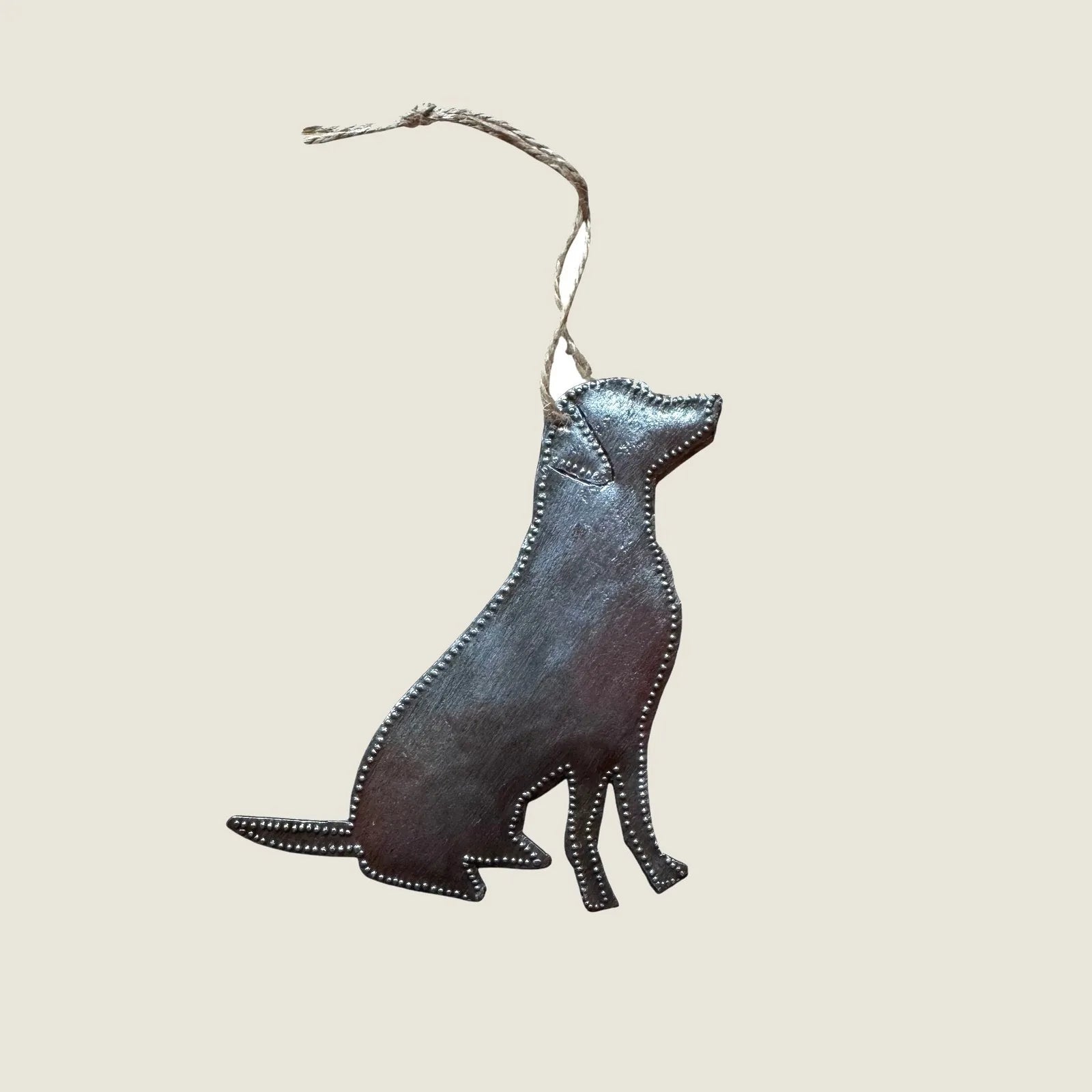 Handcrafted metal dog ornament with a sitting silhouette, featuring a rustic finish and twine for hanging.