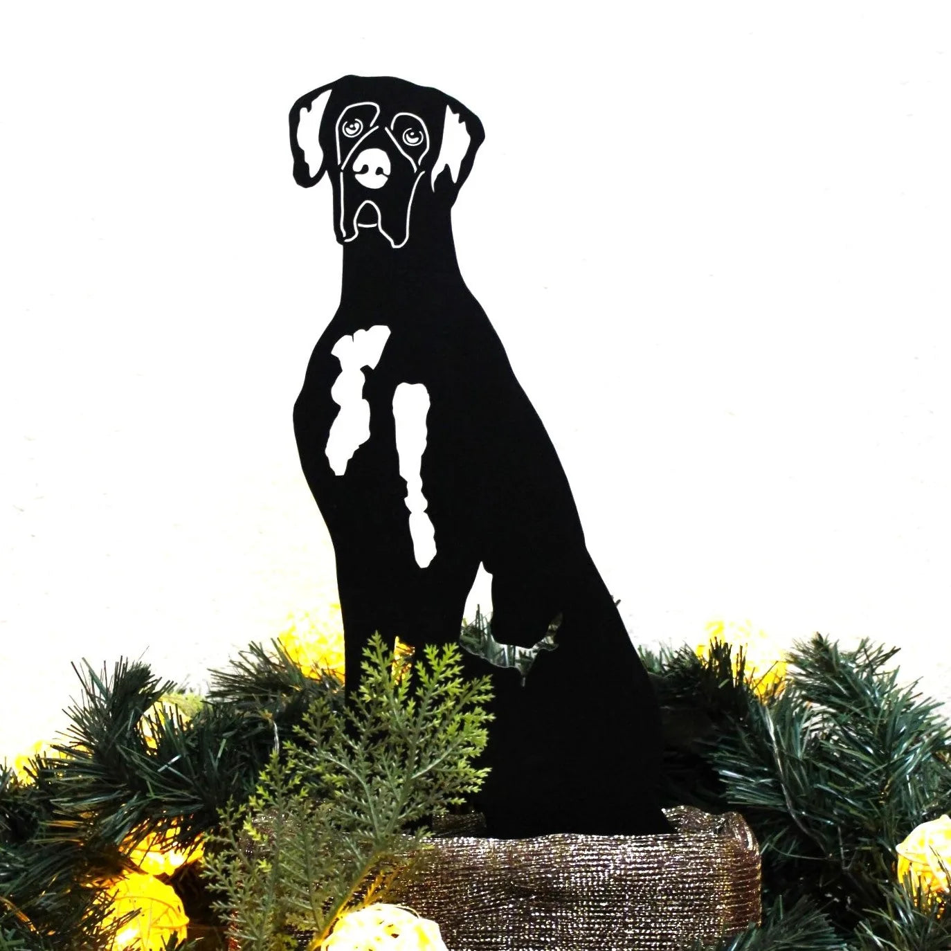 Black metal Great Dane silhouette sitting among greenery and festive decor, showcasing detailed craftsmanship.