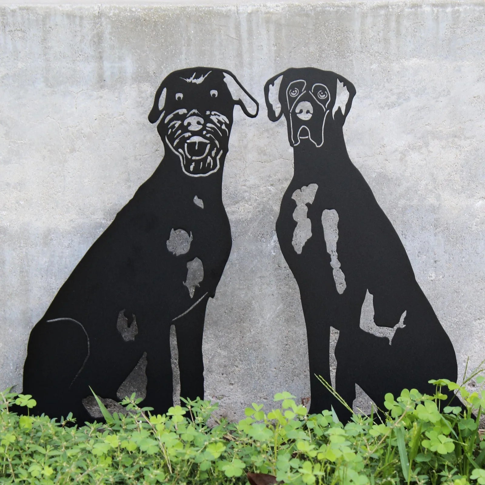Black metal dog silhouettes of two seated dogs, showcasing intricate details against a stone backdrop.