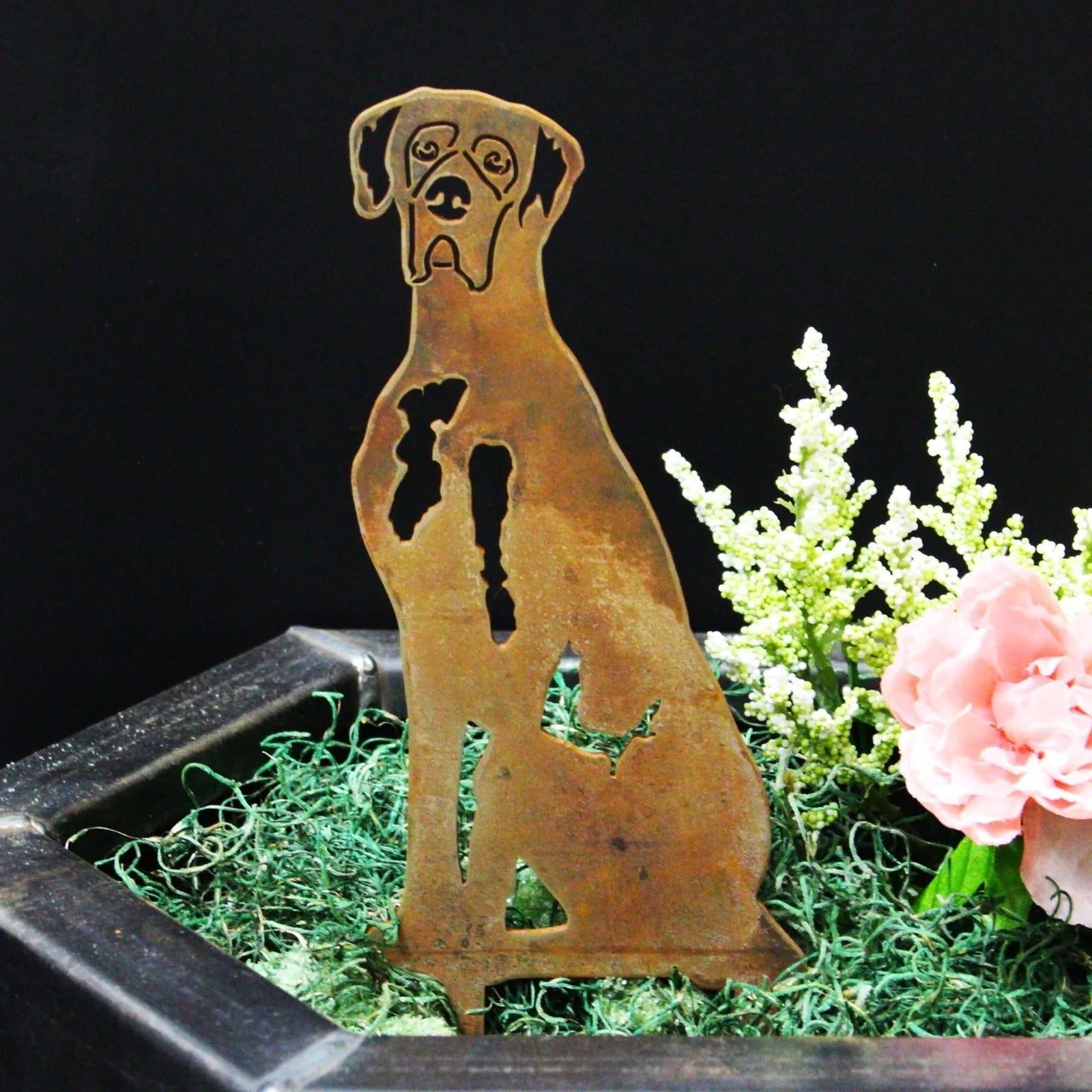 Great Dane silhouette in weathered Corten steel, displayed among greenery and flowers in a decorative planter.