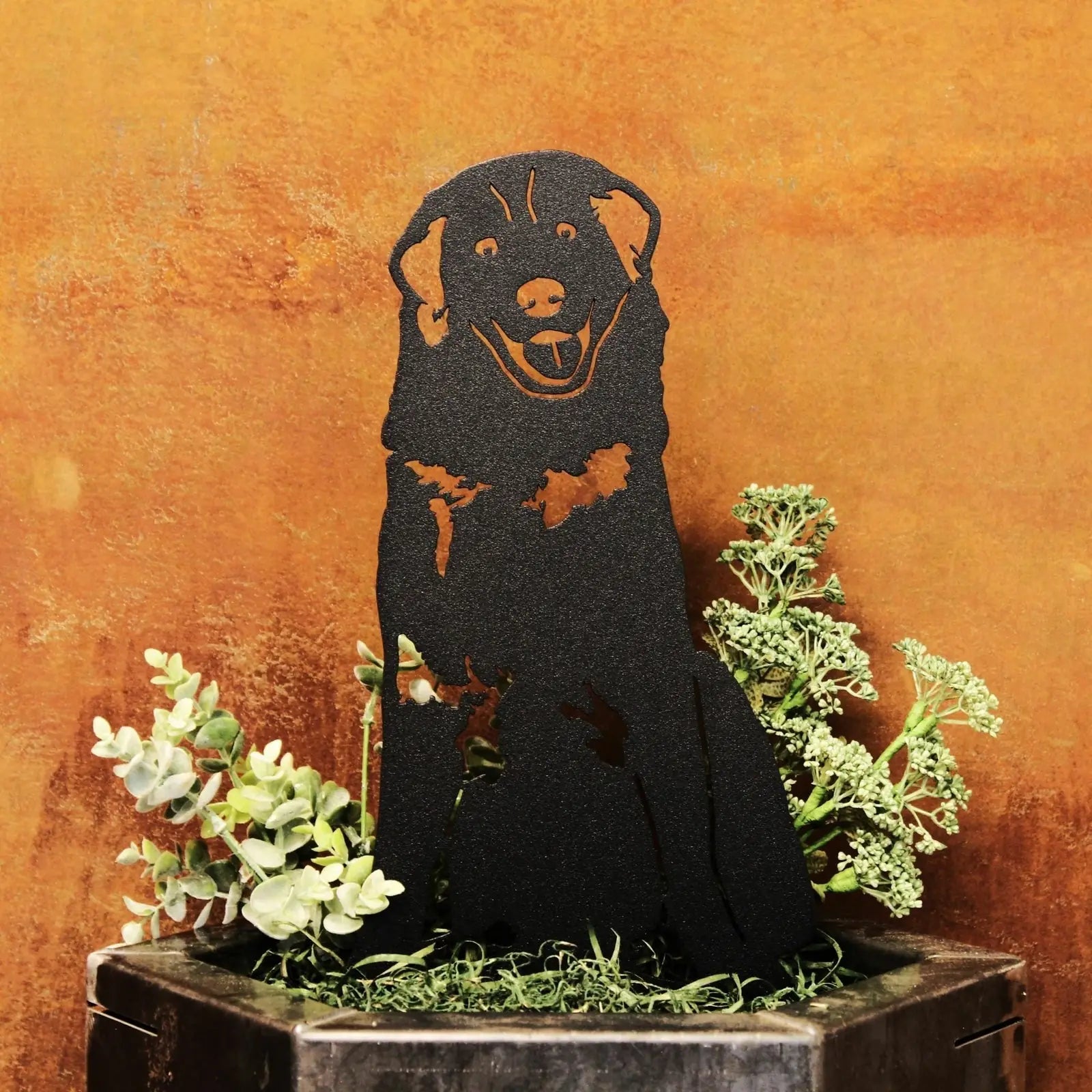 Black Great Pyrenees metal silhouette art with a smiling expression, set among greenery in a rustic setting.