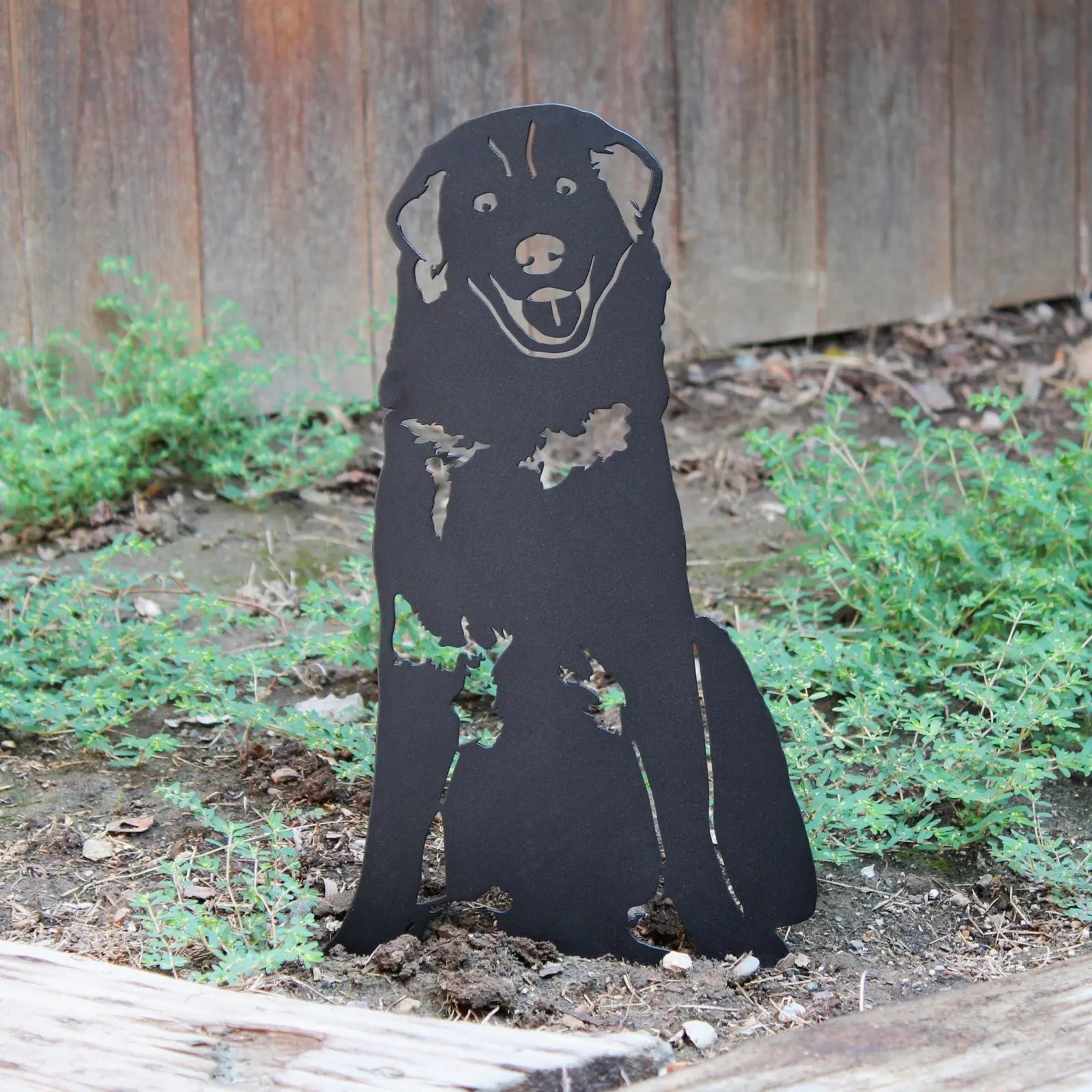 Black metal silhouette of a Great Pyrenees, showcasing a joyful expression, set among greenery in an outdoor space.