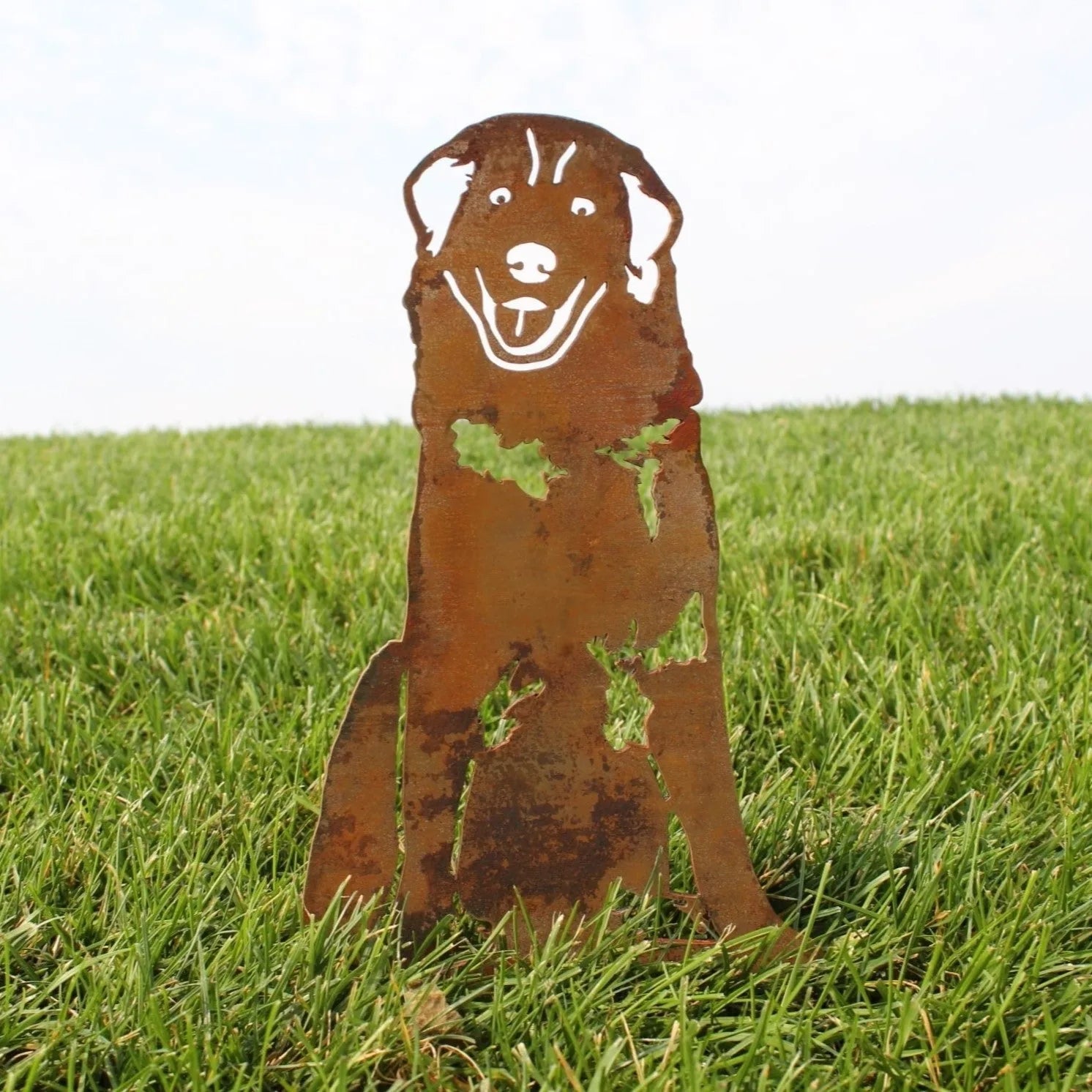 Great Pyrenees metal silhouette in weathered brown Corten steel, set against vibrant green grass.