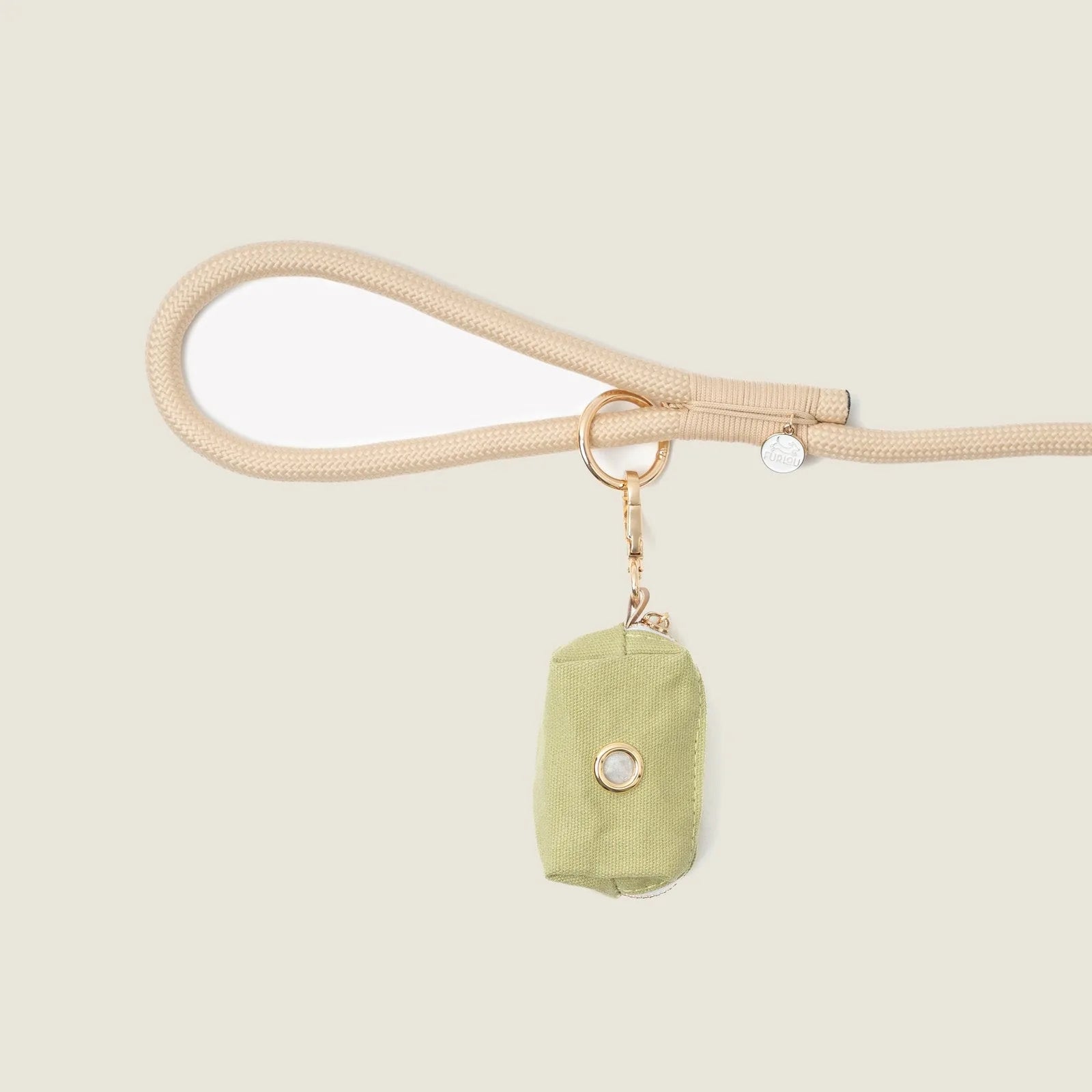 Green fabric poop bag holder clipped to a beige leash, featuring a gold hardware detail for easy access.