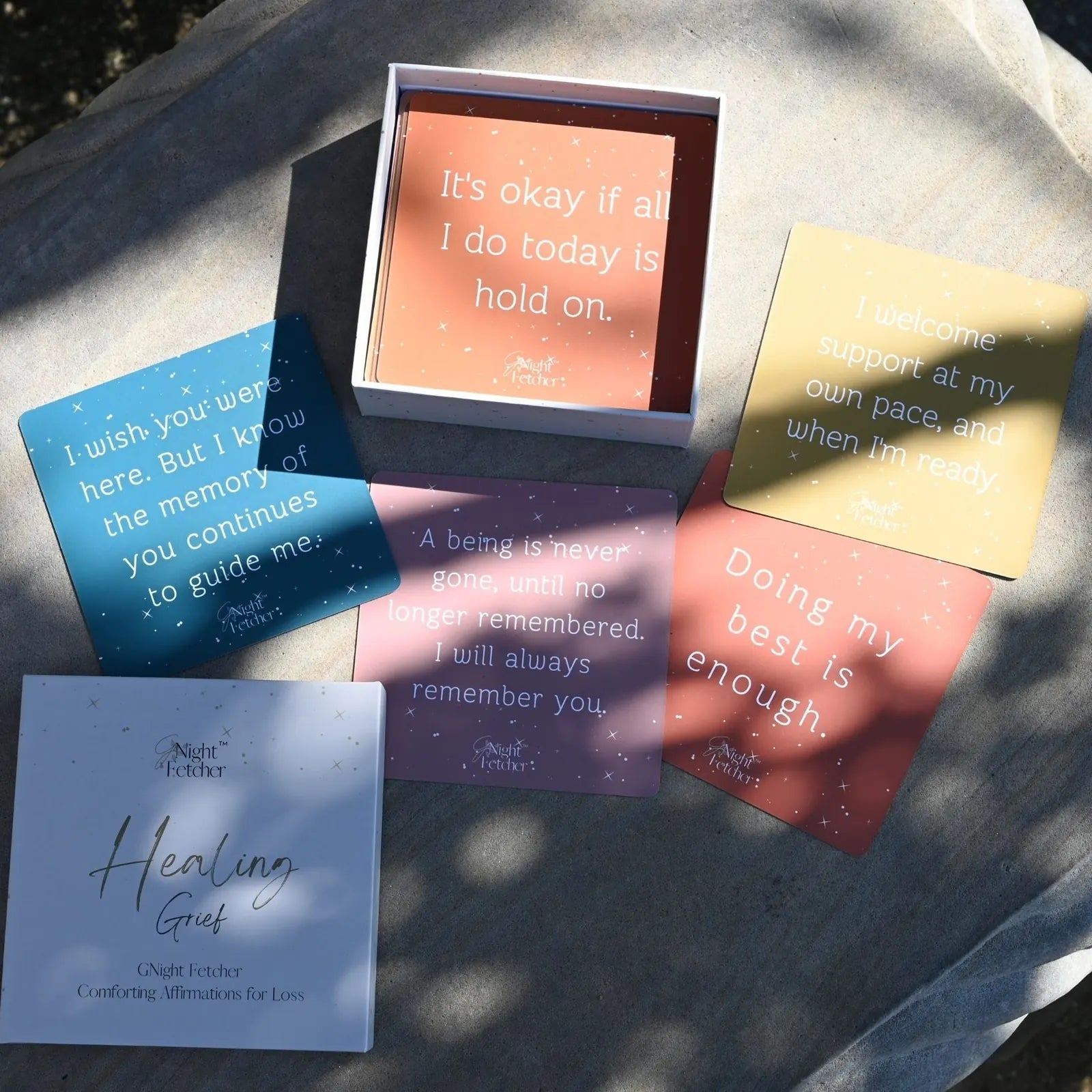 Grief affirmation cards with soothing messages, in pastel colors, displayed in a box on a textured surface.