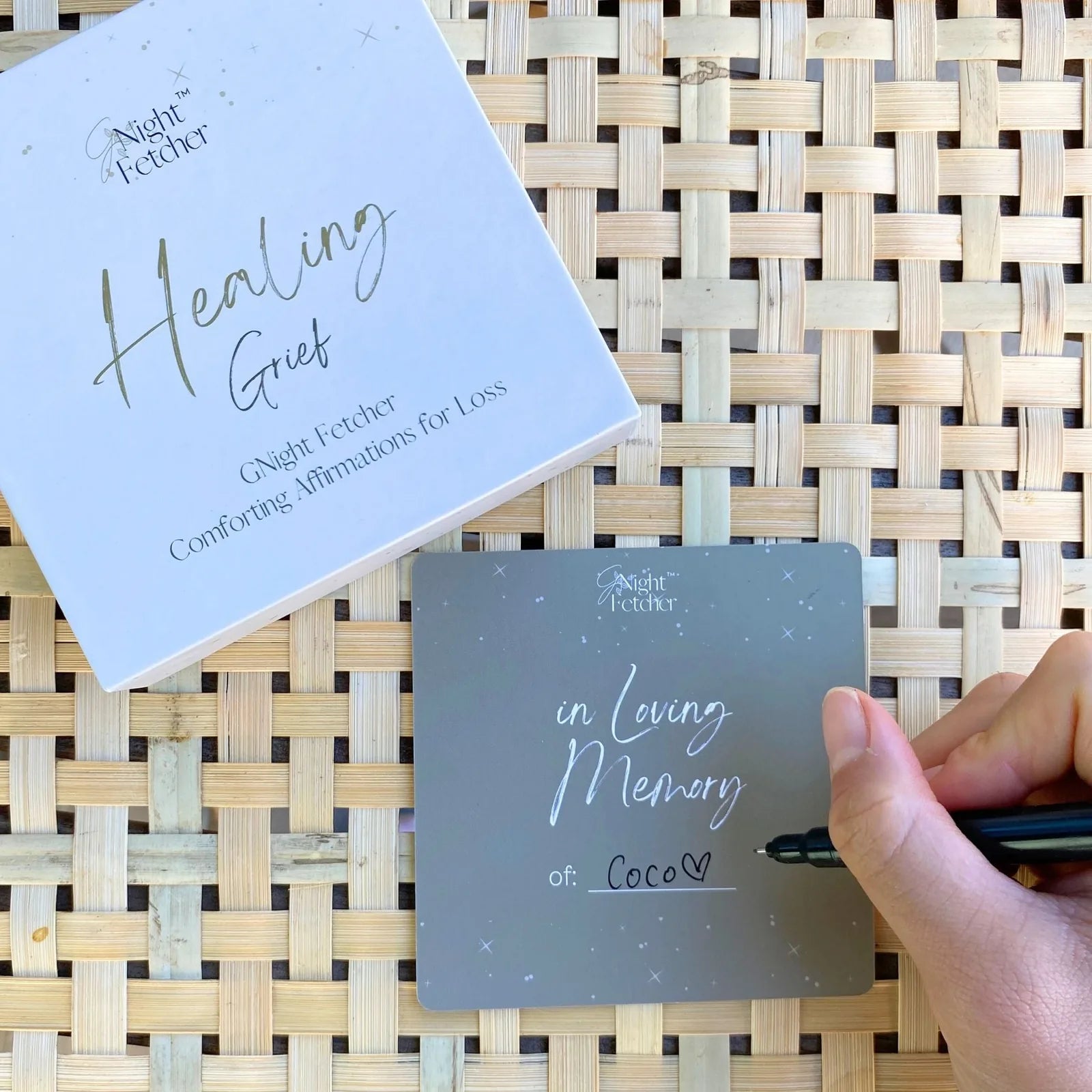 Grief Affirmation Card with "in Loving Memory of: Coco" written, resting on a woven surface. Healing Grief box nearby.