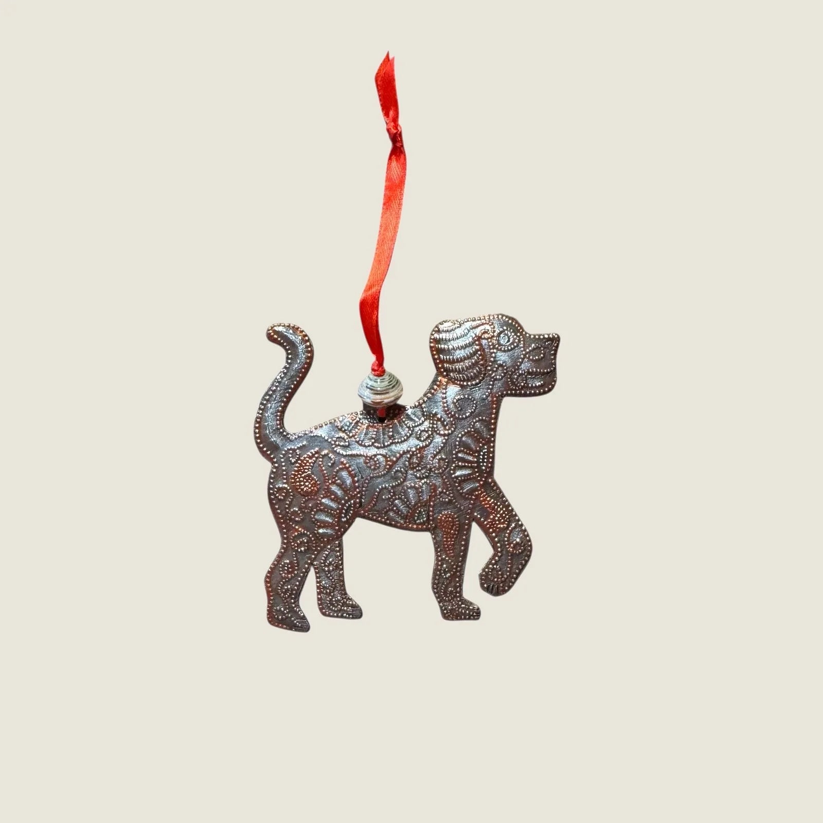 Handcrafted bronze dog ornament with intricate patterns, hanging from a red ribbon. A unique piece for dog lovers.