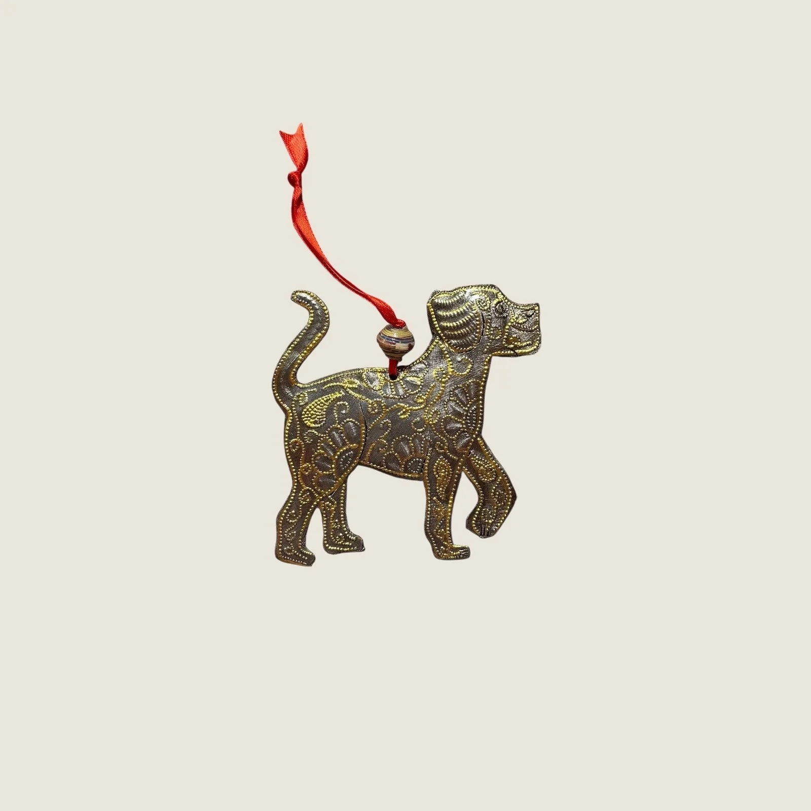 Handcrafted gold dog ornament with intricate designs, suspended by a red ribbon, perfect for home decor.