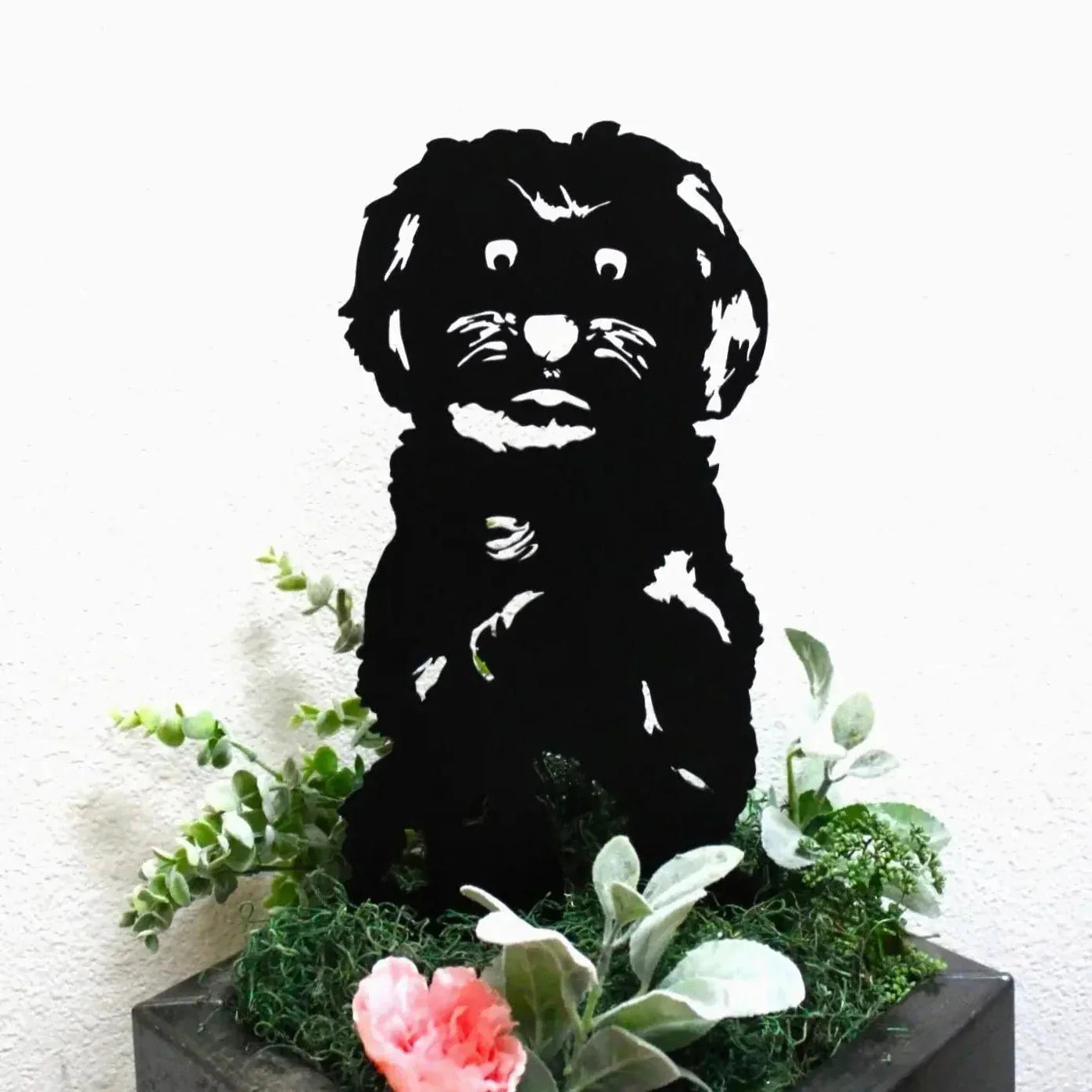 Black Havanese dog silhouette art placed in greenery with flowers, showcasing intricate detailing in a modern metal design.