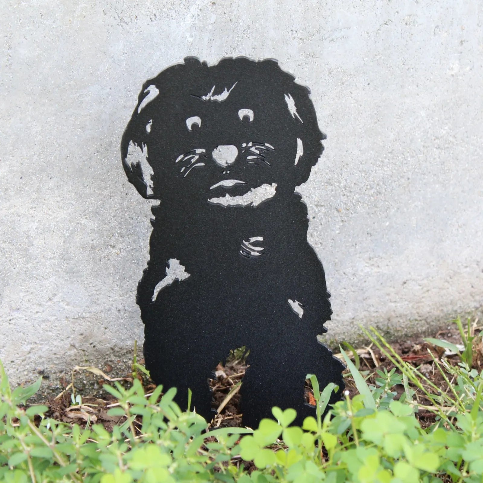 Black metal silhouette of a Havanese dog standing in green grass against a textured gray background.