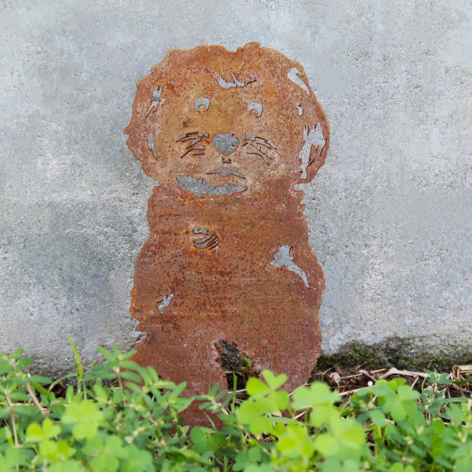 Rust-colored Havanese metal silhouette, handcrafted from weathering steel, surrounded by green foliage.