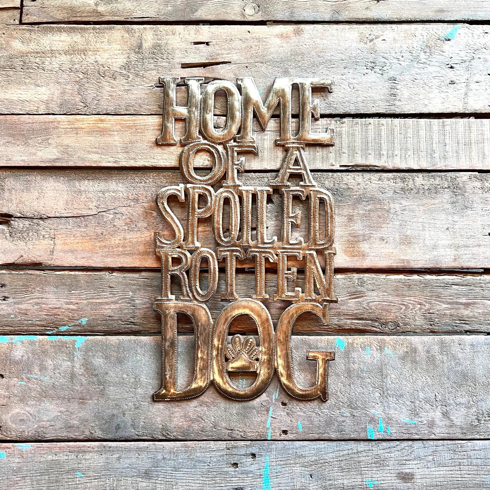 Handcrafted metal wall art reads "Home of a Spoiled Rotten Dog" with a paw print design, set against rustic wood.
