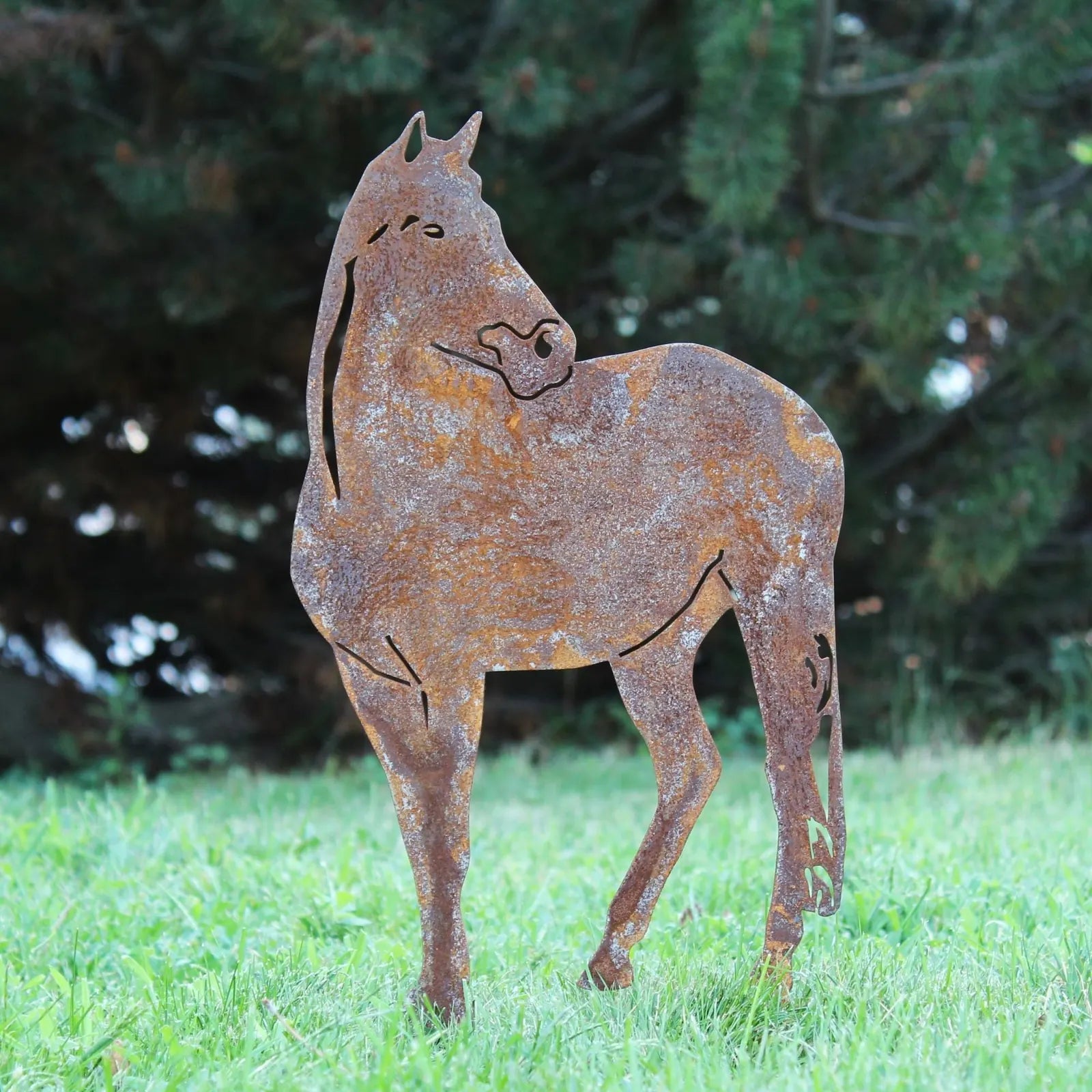 Rusty horse silhouette crafted from Corten steel, standing on grass with trees in the background, perfect for outdoor decor.