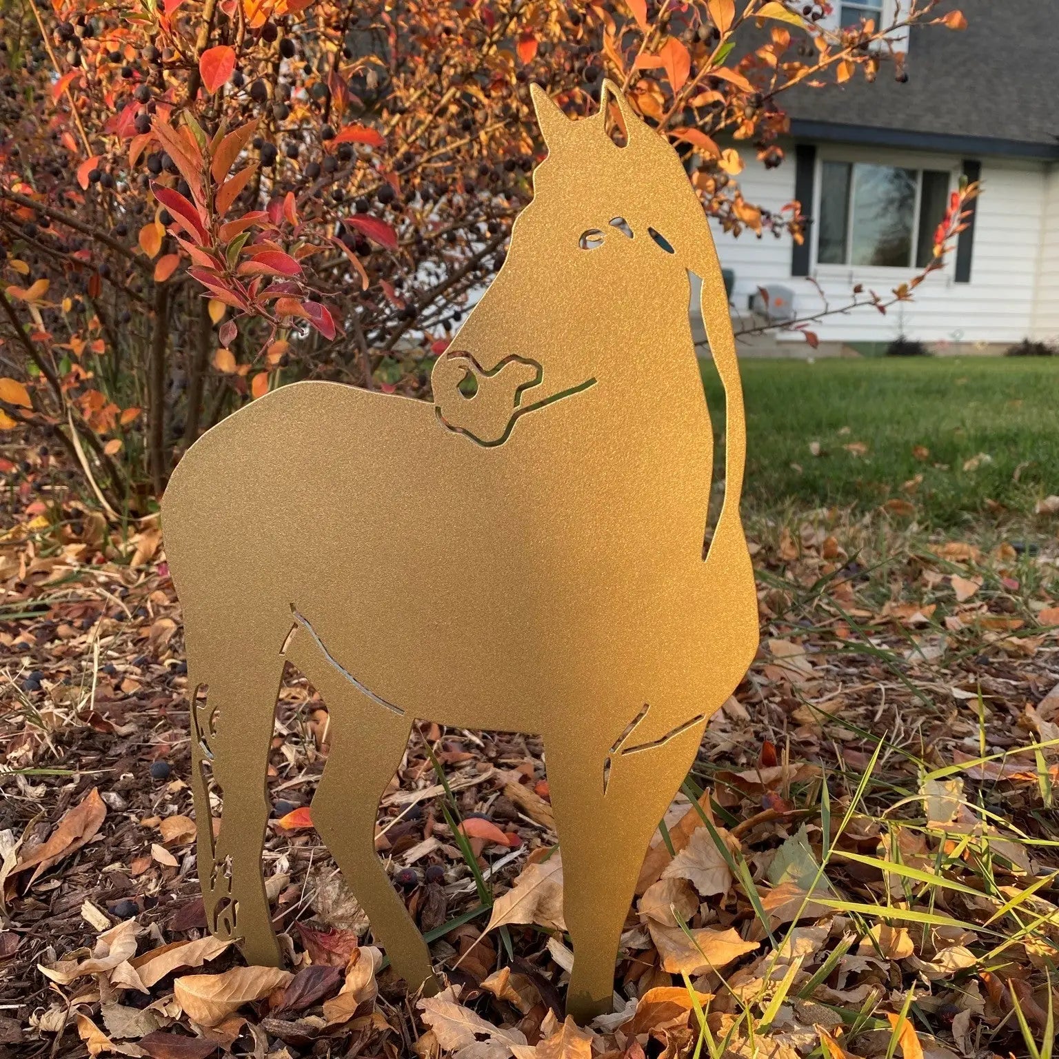 Gold horse silhouette metal wall art set in a garden among autumn leaves, showcasing a rustic outdoor decor style.