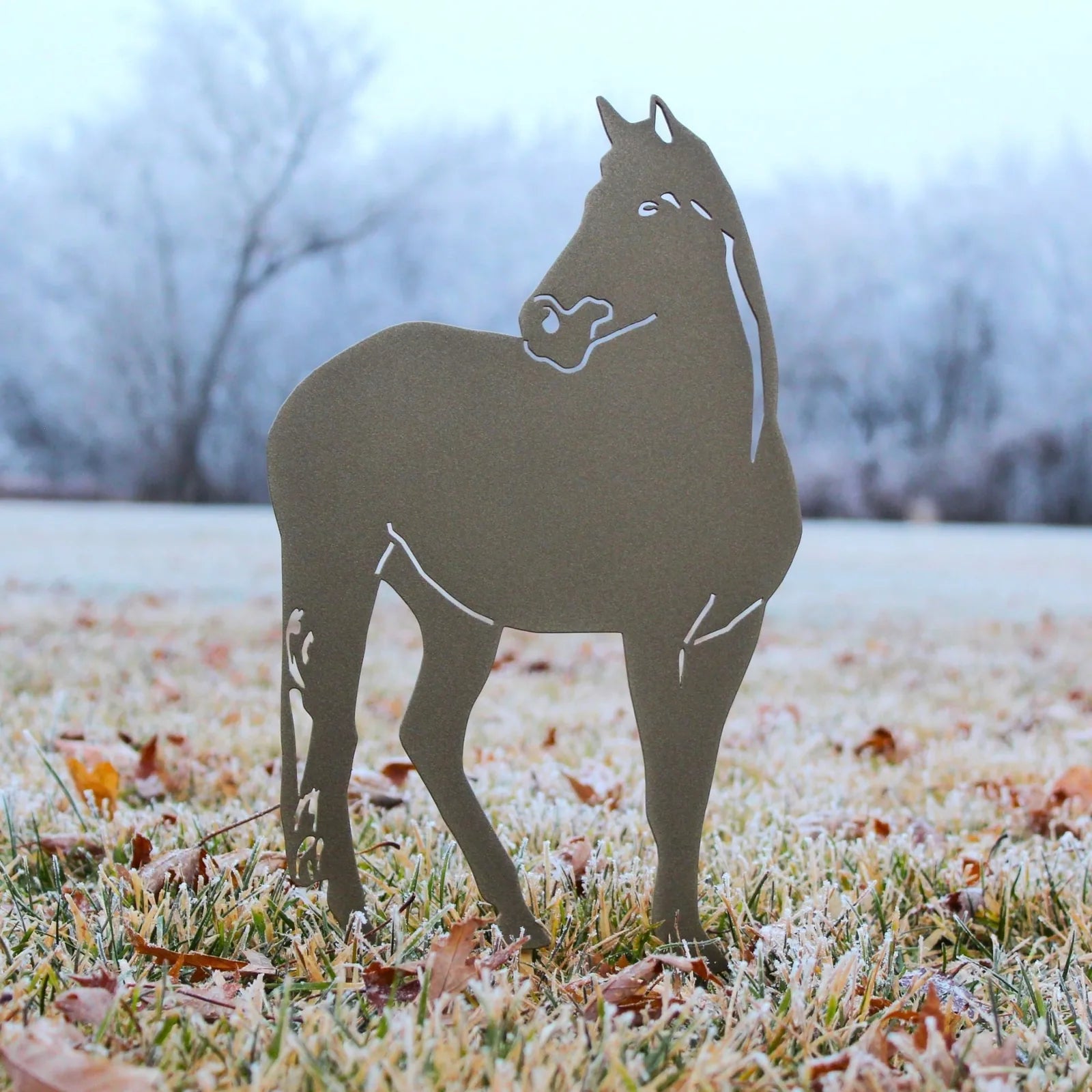 Corten steel horse silhouette stands on frosted grass, featuring a rustic design perfect for outdoor decor.
