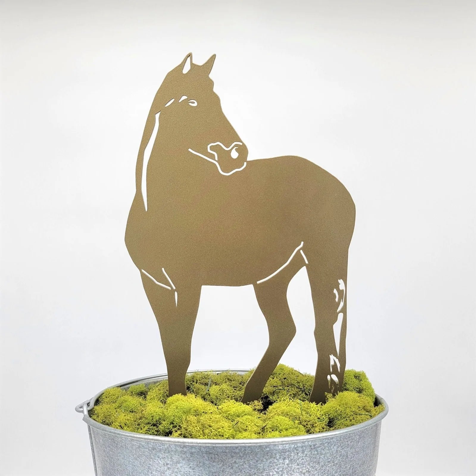 Gold horse silhouette made of metal with intricate detailing, displayed in a pot of green moss.