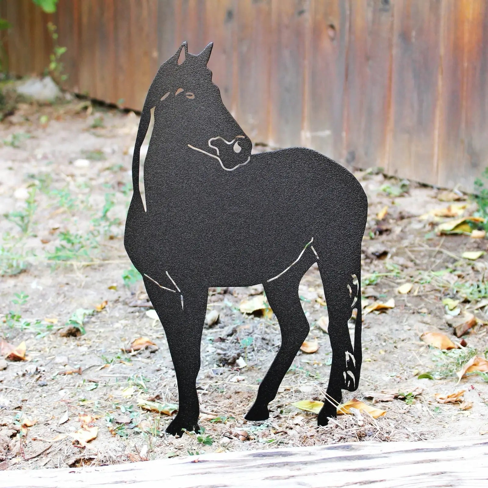 Black metal horse silhouette standing in a garden setting, showcasing intricate detailing and natural surroundings.