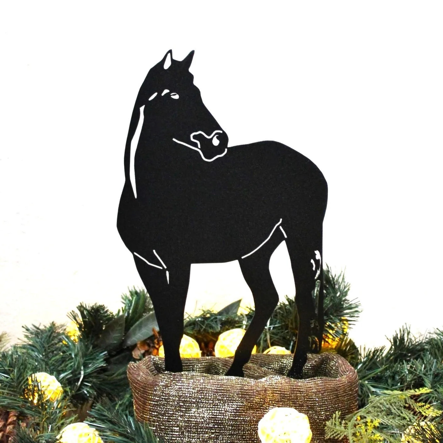 Black horse silhouette wall art placed atop a decorative base with greenery and lights, highlighting its artistic design.
