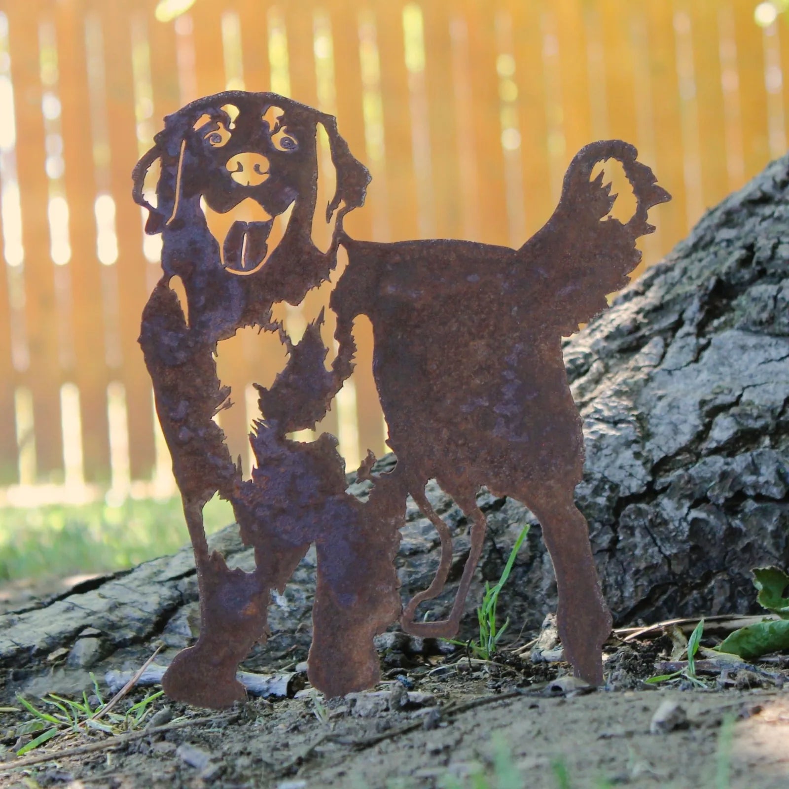 Rusty Hovawart dog silhouette made of Corten steel, positioned near a tree with a blurred wooden fence in the background.