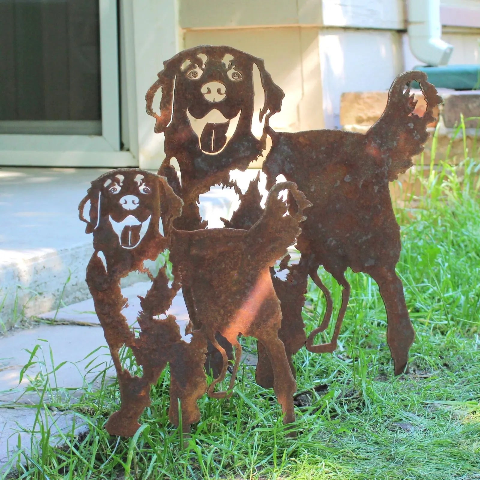Rusty metal silhouette of two Hovawart dogs, handmade from Corten steel, set in grass near a patio.