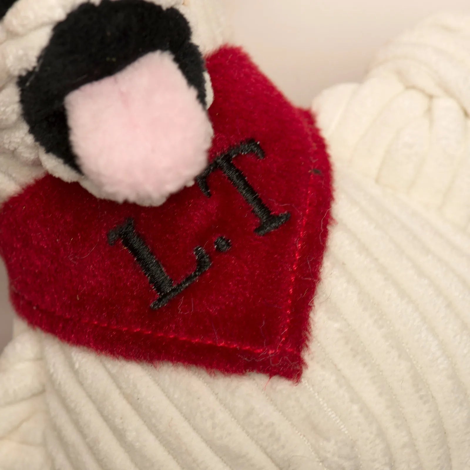 Soft white plush dog toy with a red heart-shaped patch reading "L.T." and a black and pink snout.