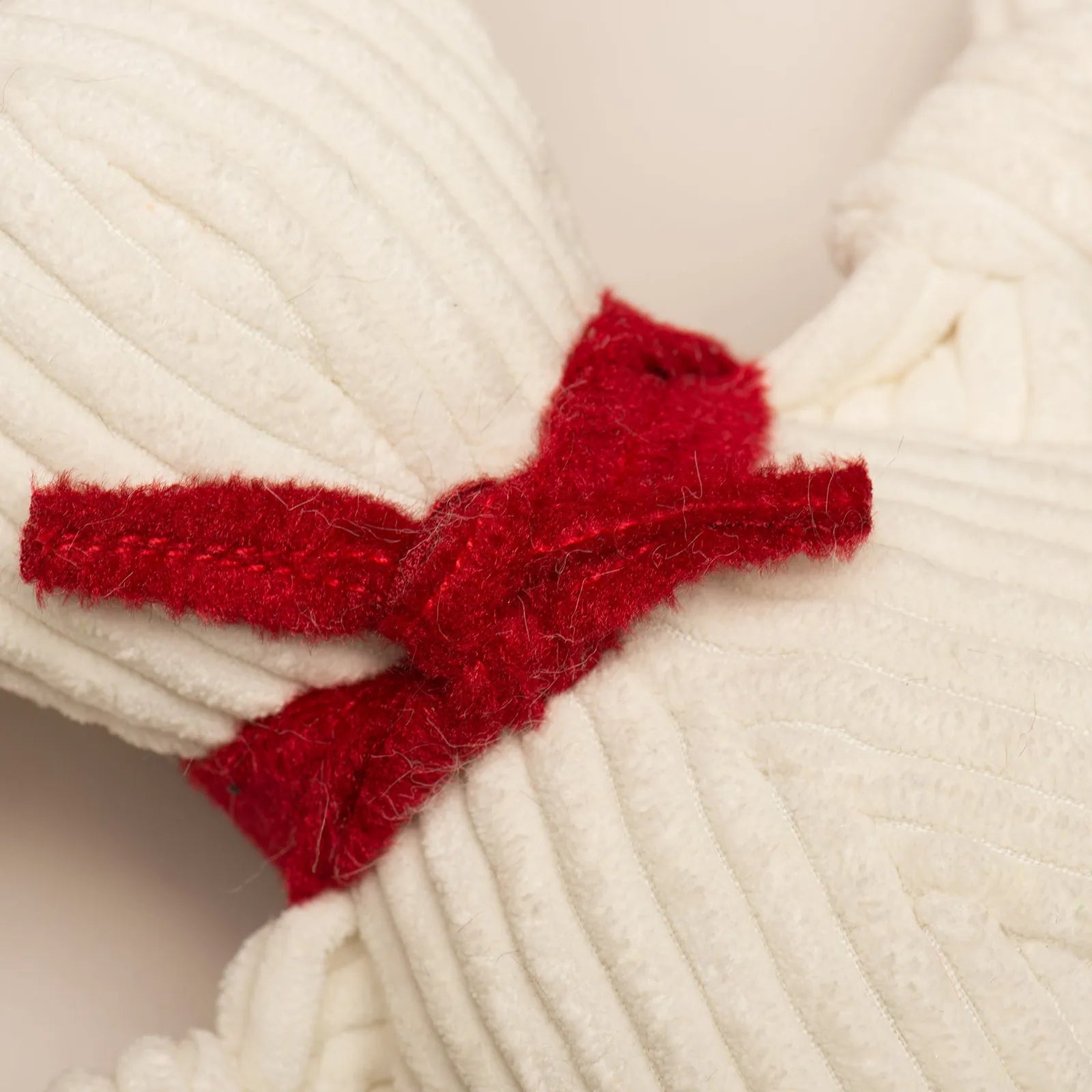 Cream-colored plush dog toy with a red knotted accent, designed for playful tugging and chewing.