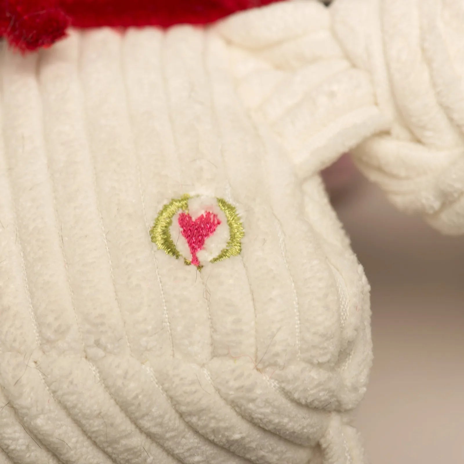 Close-up of the HuggleCause™ L.T. Knottie® plush toy showing soft white fabric with a heart logo in pink and green.