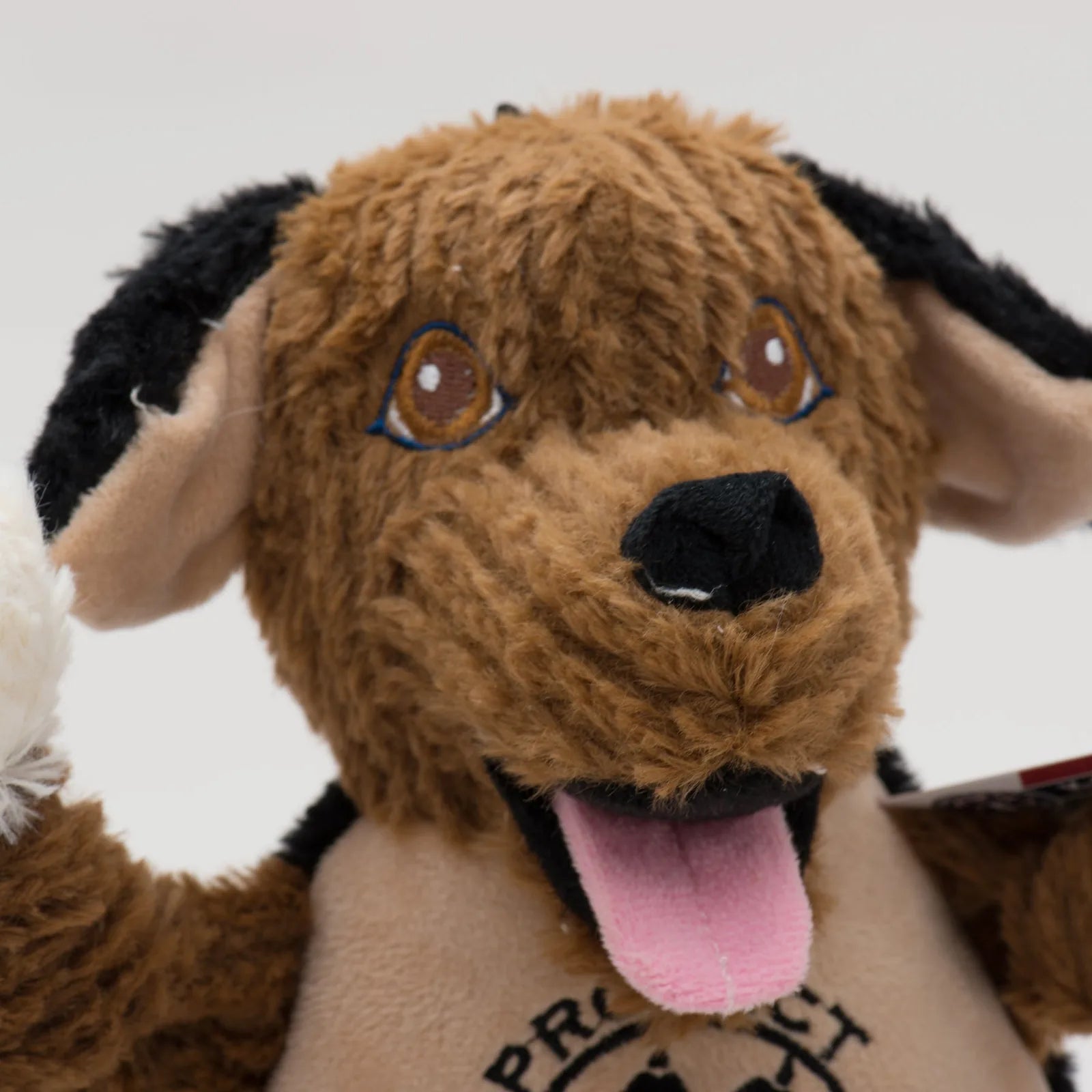 Plush dog toy depicting a friendly, brown canine with floppy ears, a joyful expression, and a logo on its body.