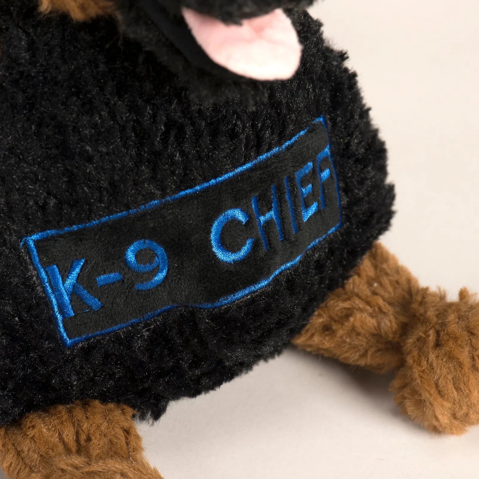 K-9 Chief Knottie plush dog toy featuring black fur, a blue embroidered badge, and brown limbs, ideal for interactive play.