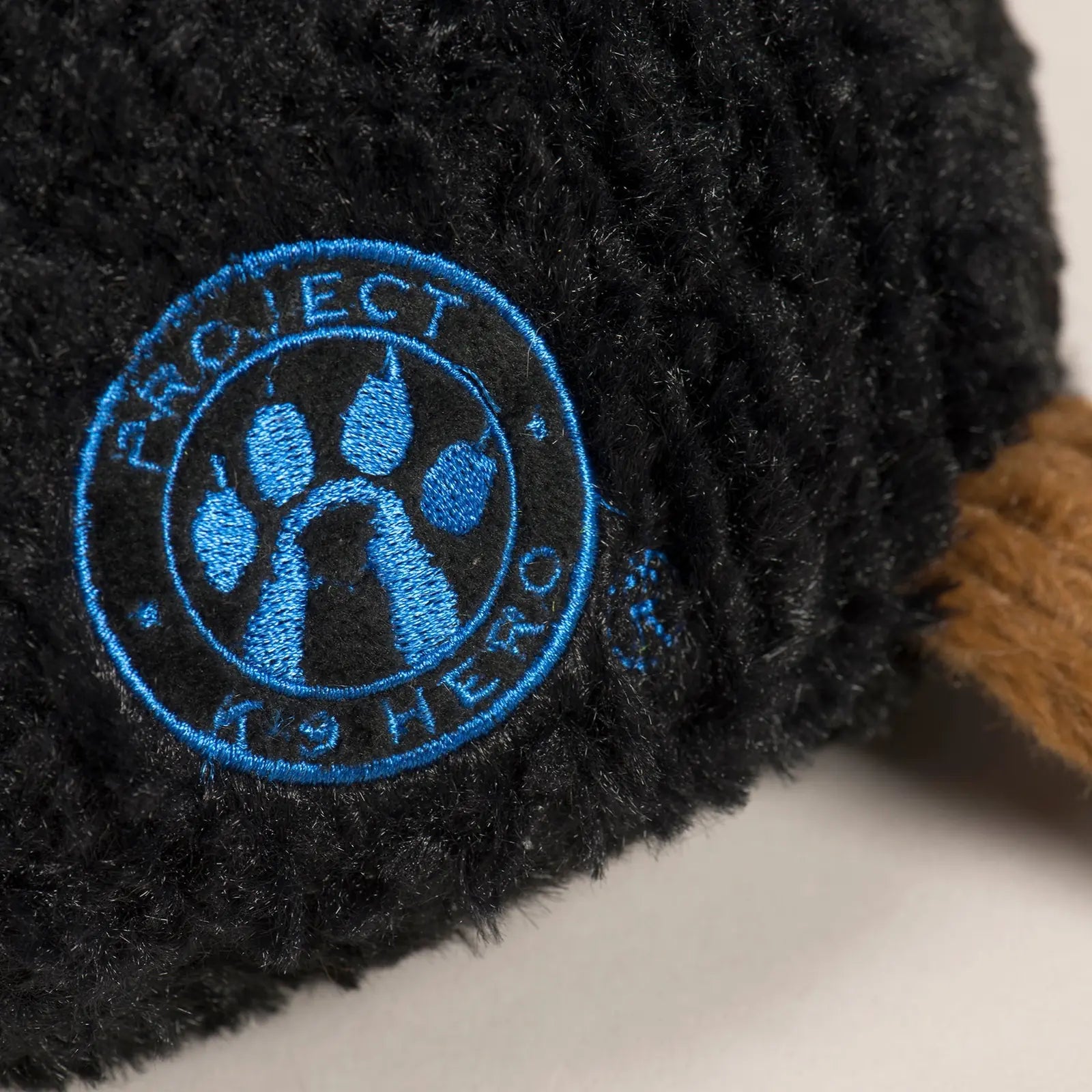 Embroidered blue "Project K-9 Hero" logo on a black, plush dog toy with a brown knotted limb.