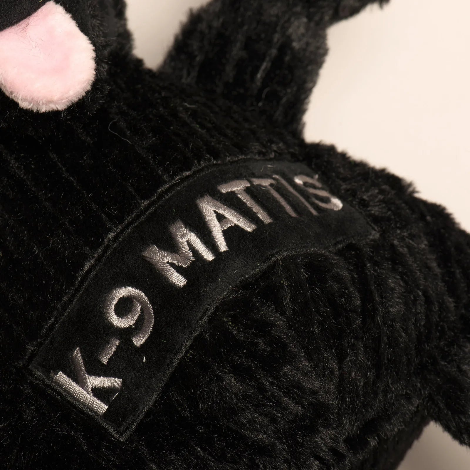 Large black plush dog toy featuring "K-9 MATTIS" embroidery, designed for durability and interactive play.