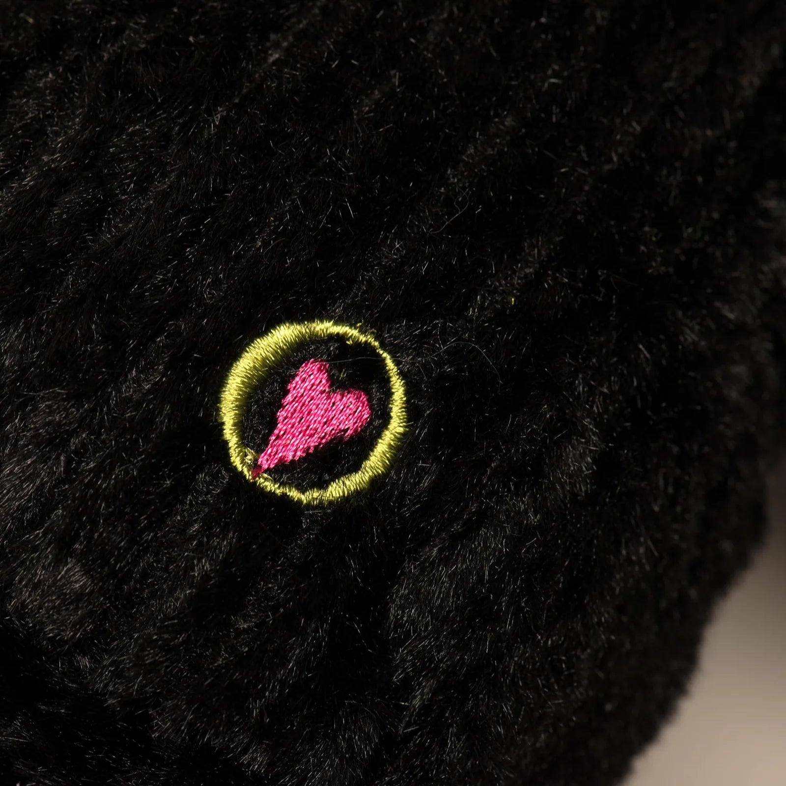 Black plush fabric featuring an embroidered pink heart within a yellow circle, highlighting durability and design.