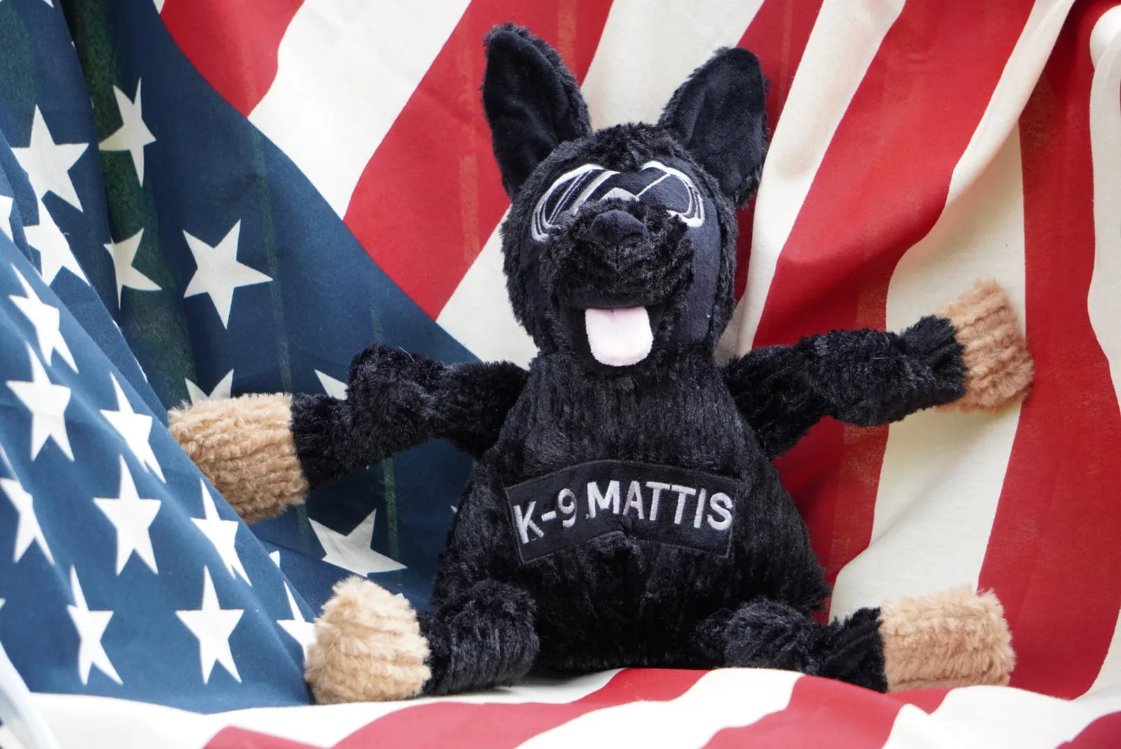 Large black plush dog toy shaped like a German Shepherd with knotted limbs, featuring "K-9 MATTIS" on its belly against an...