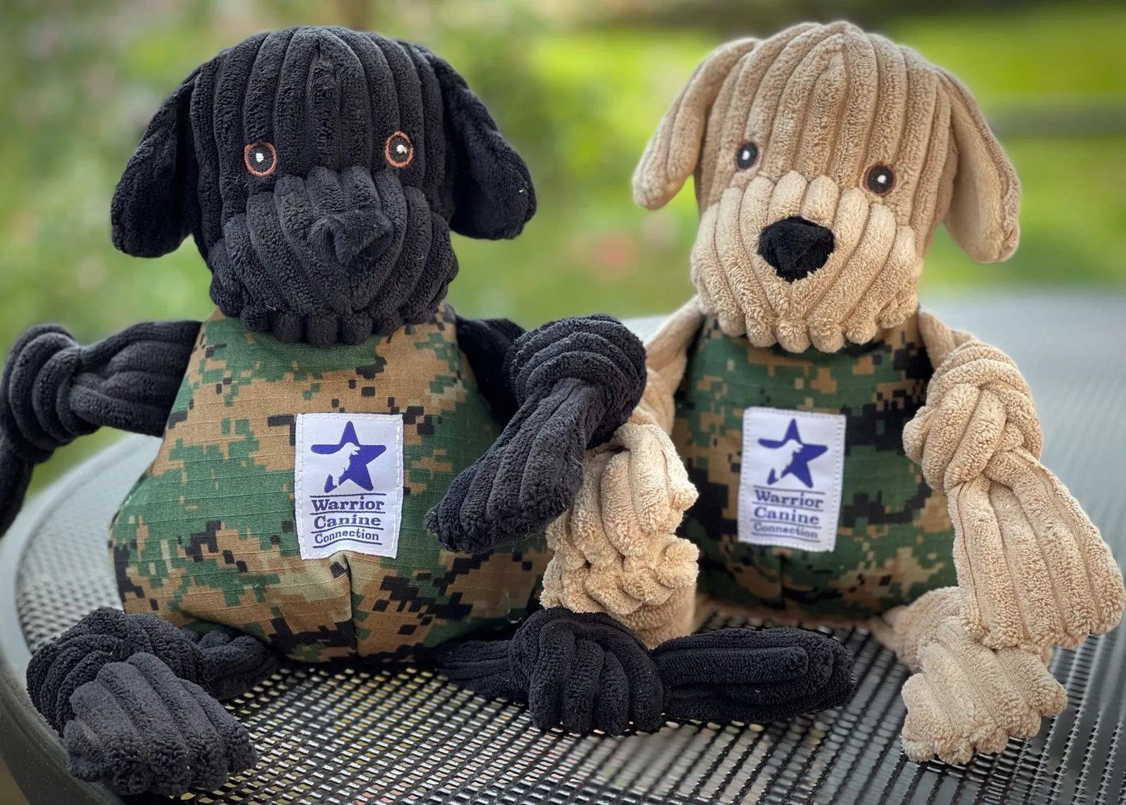 Large black and tan plush dog toys, with knotted limbs and military-style vests, supporting the Warrior Canine Connection.